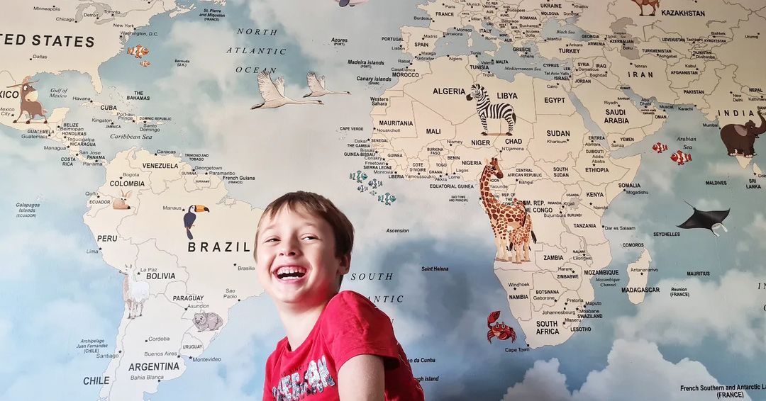 Bambino sorridente davanti a una mappa del mondo con illustrazioni di animali.