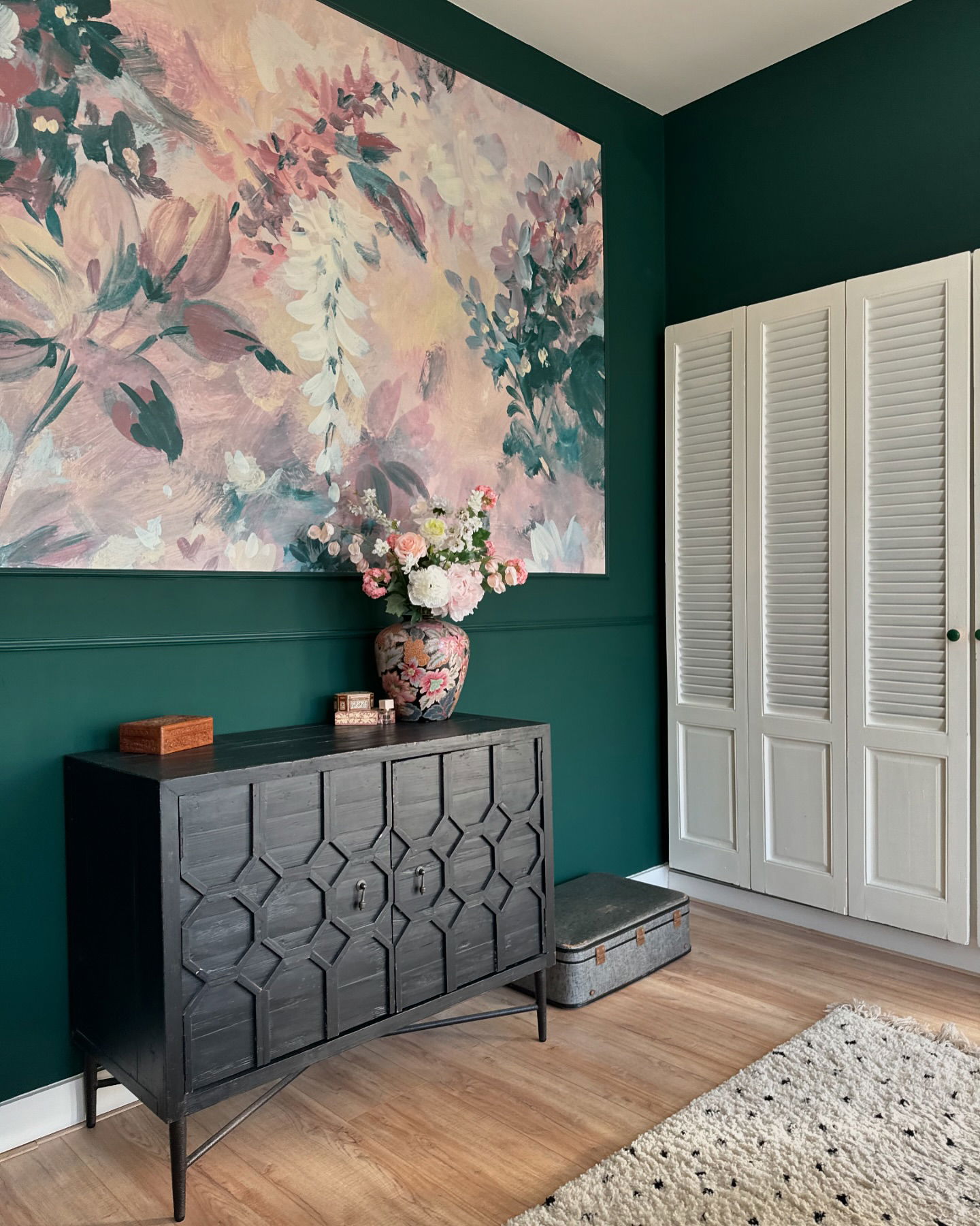 Interieur met donkergroene muren, zwarte kast, bloemenschilderij en witte louvrekast.