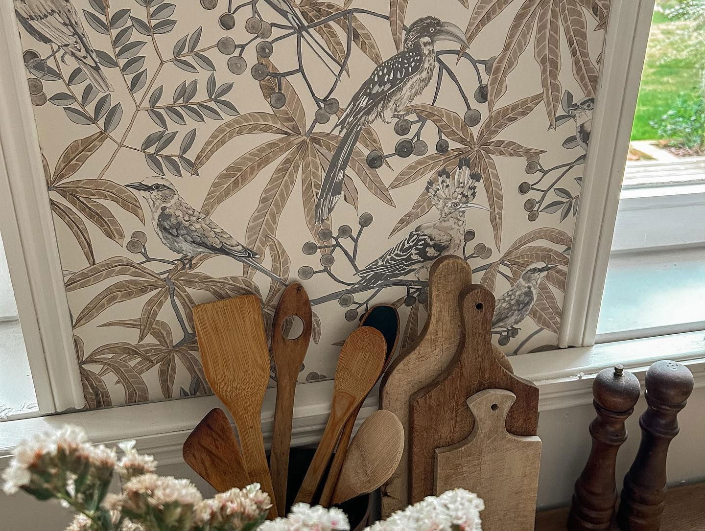 Escena de cocina con papel tapiz de pájaros, utensilios de madera y tablas de cortar.