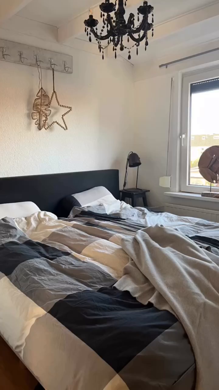 Bedroom with unmade bed, black headboard, black chandelier, and star decoration.