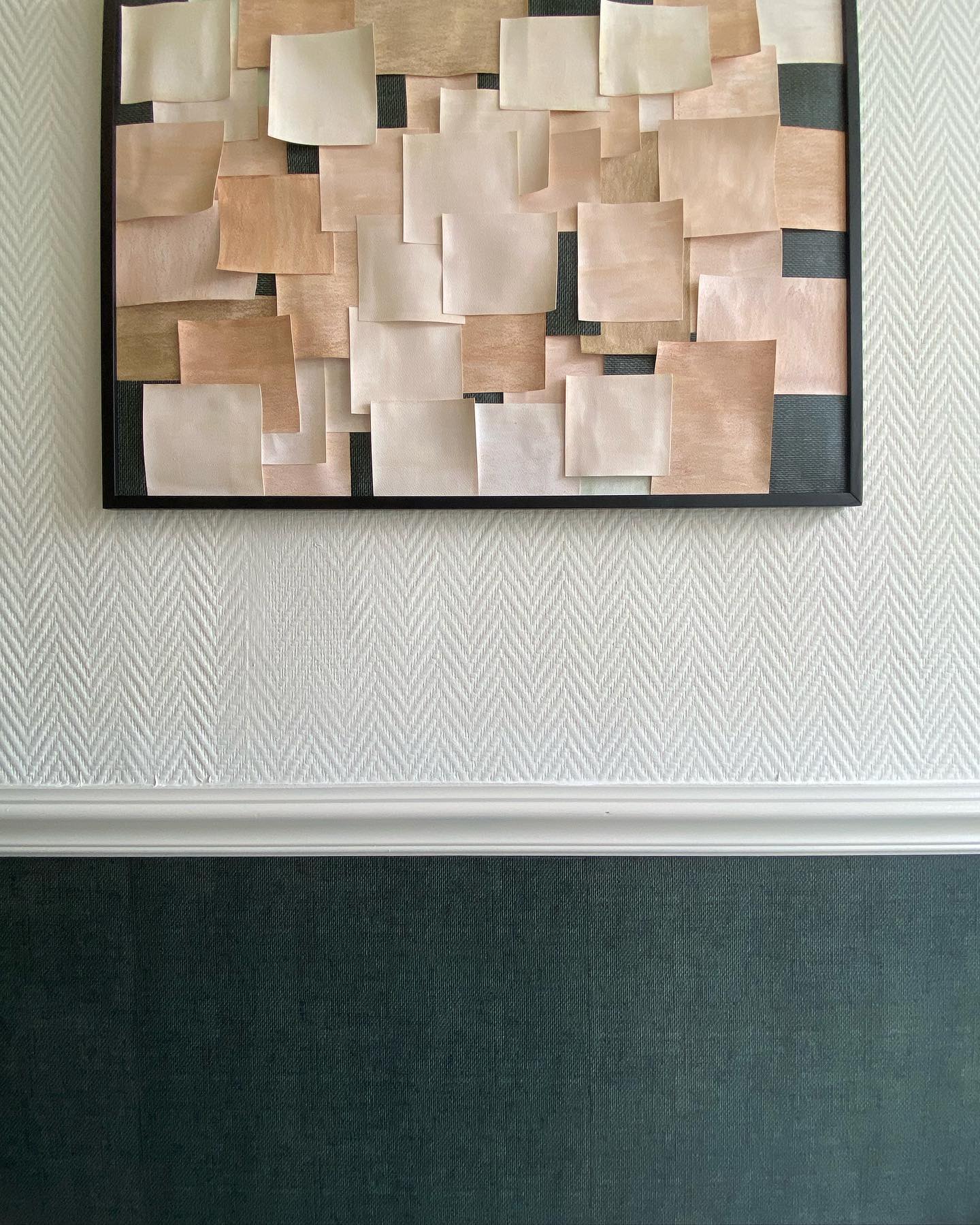 Framed collage of square paper swatches in neutral tones hangs on a herringbone wallpapered wall.