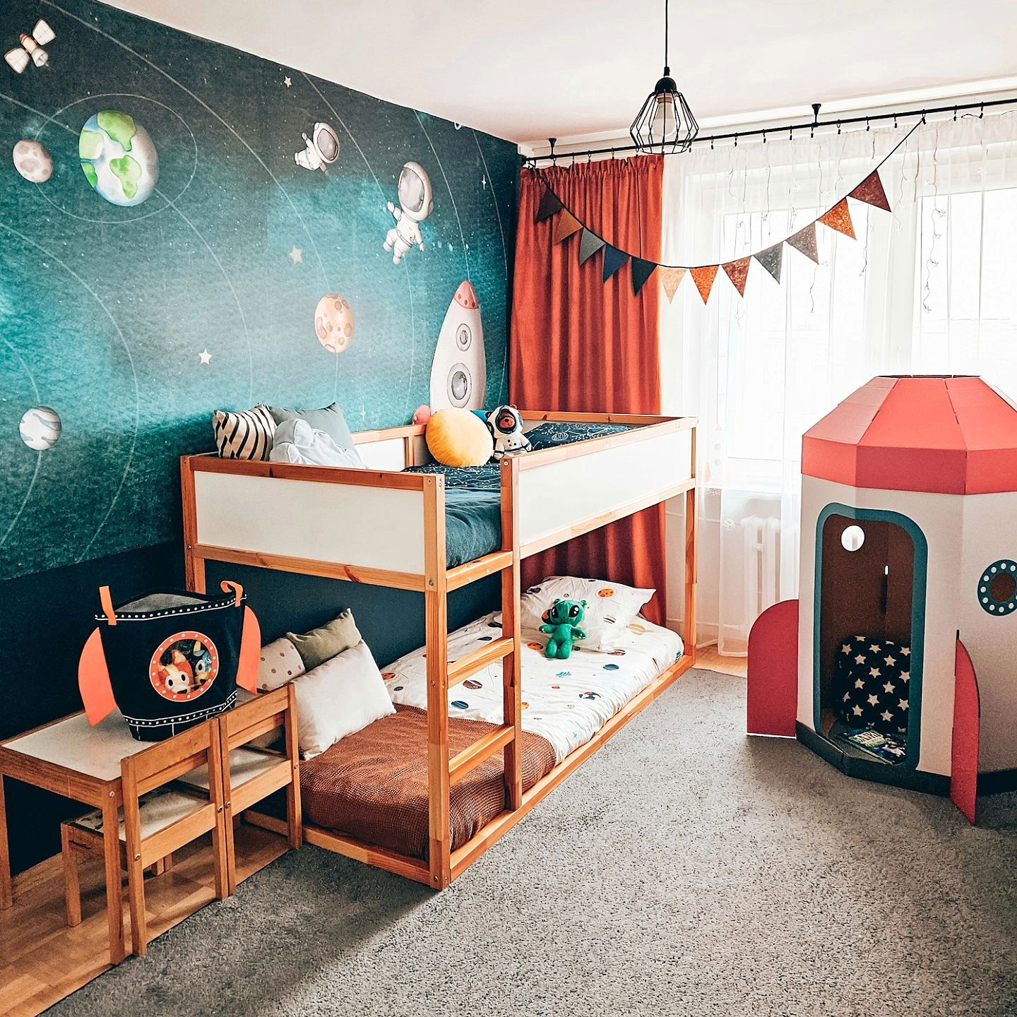 Child's bedroom with space-themed wallpaper, wooden bunk beds, and a cardboard rocket ship.