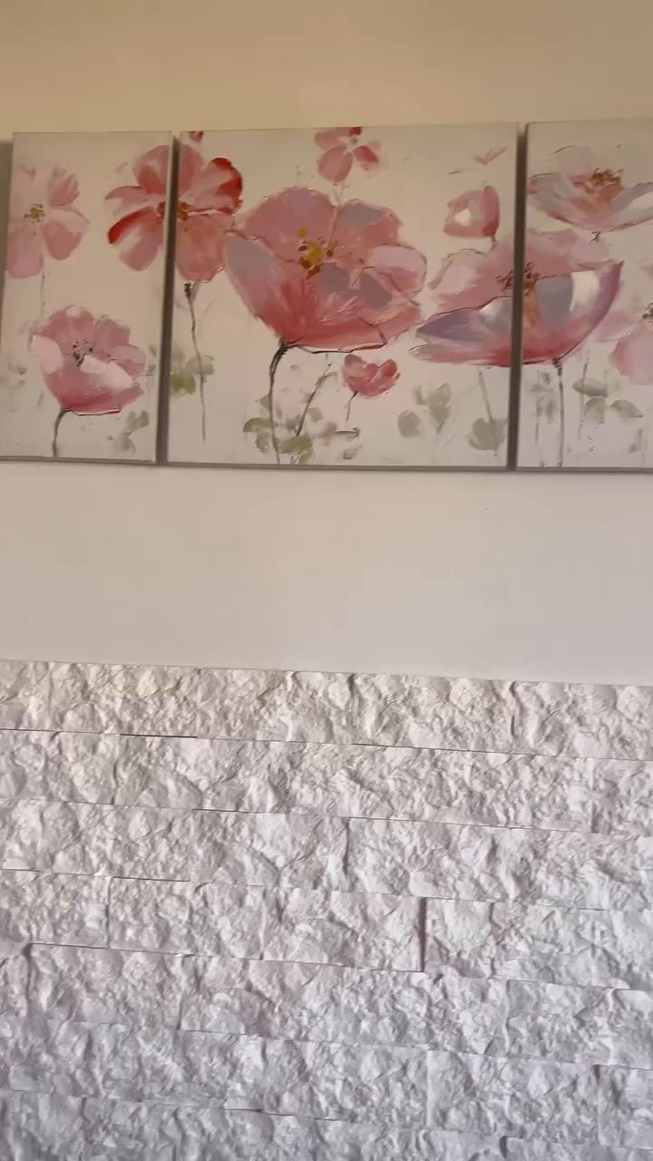 Three-panel floral painting above a white stone accent wall.