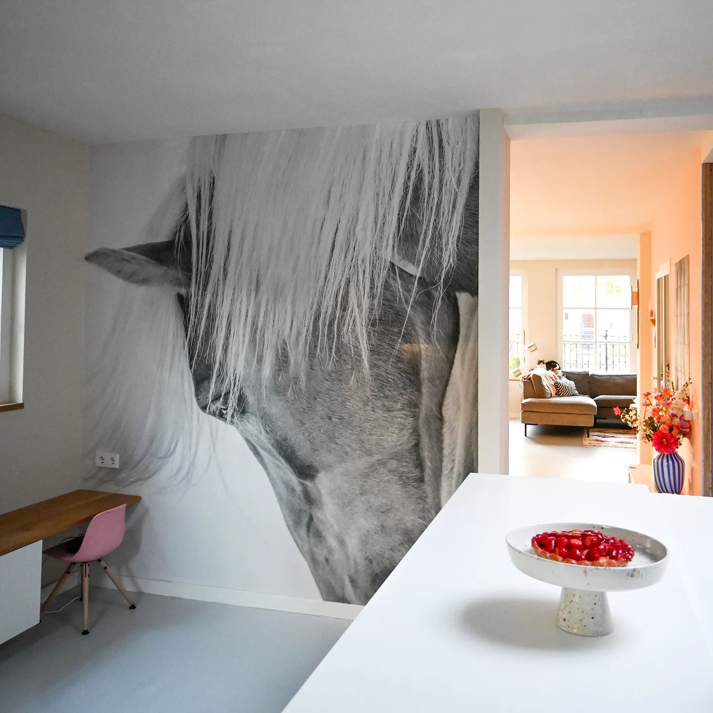 Interior view with a large horse mural, desk with pink chair, and a cake stand with a strawberry dessert.