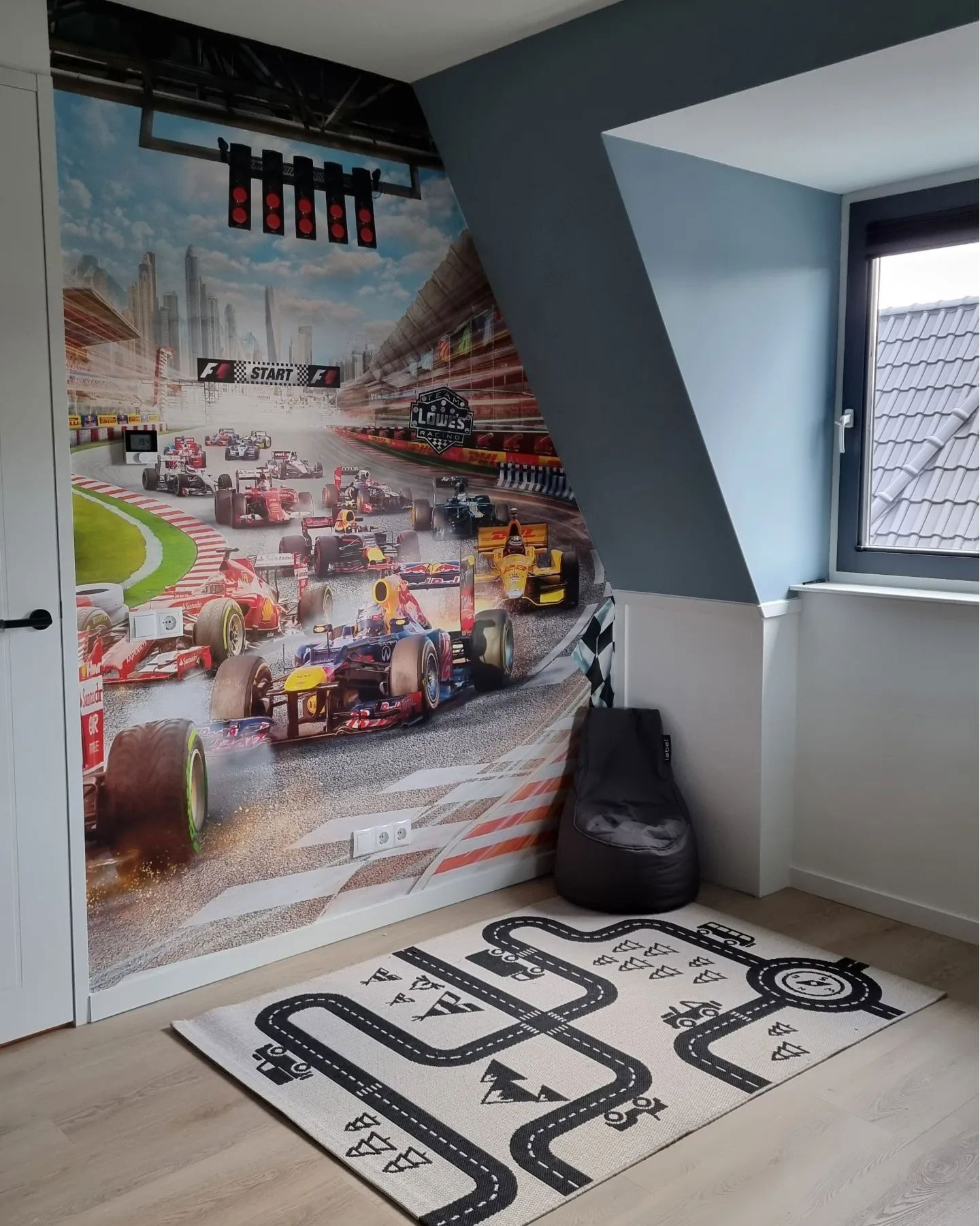 Child's room with race car wallpaper, road-themed rug, and gray beanbag chair.