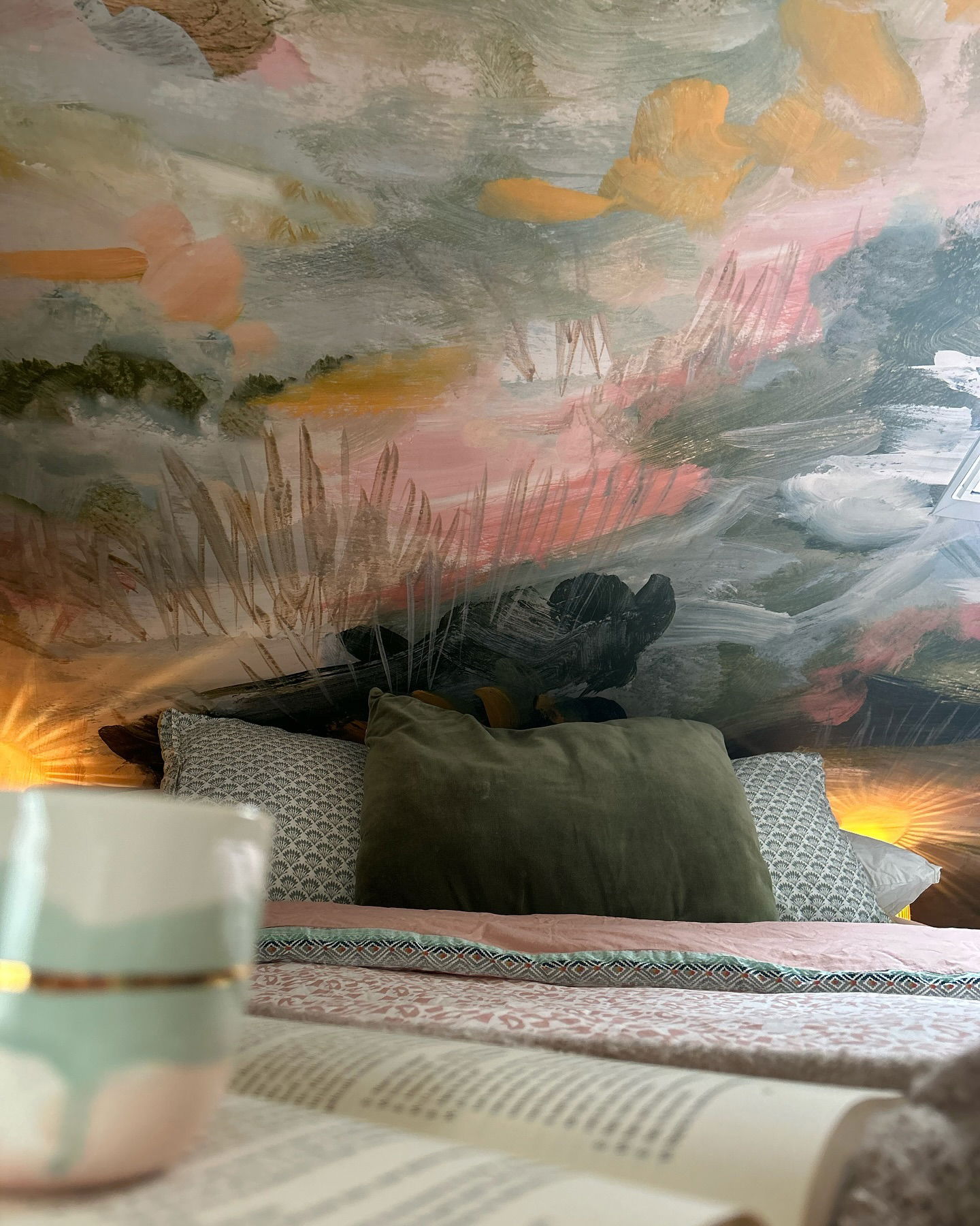 Cozy bedroom scene with painted mural, pillows, and open book.