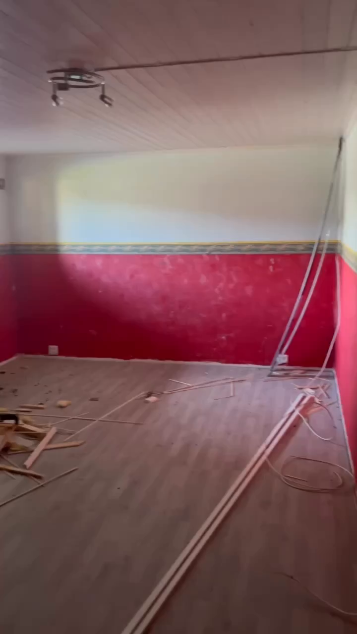 Empty room with red accent wall, wood floors, and construction debris.