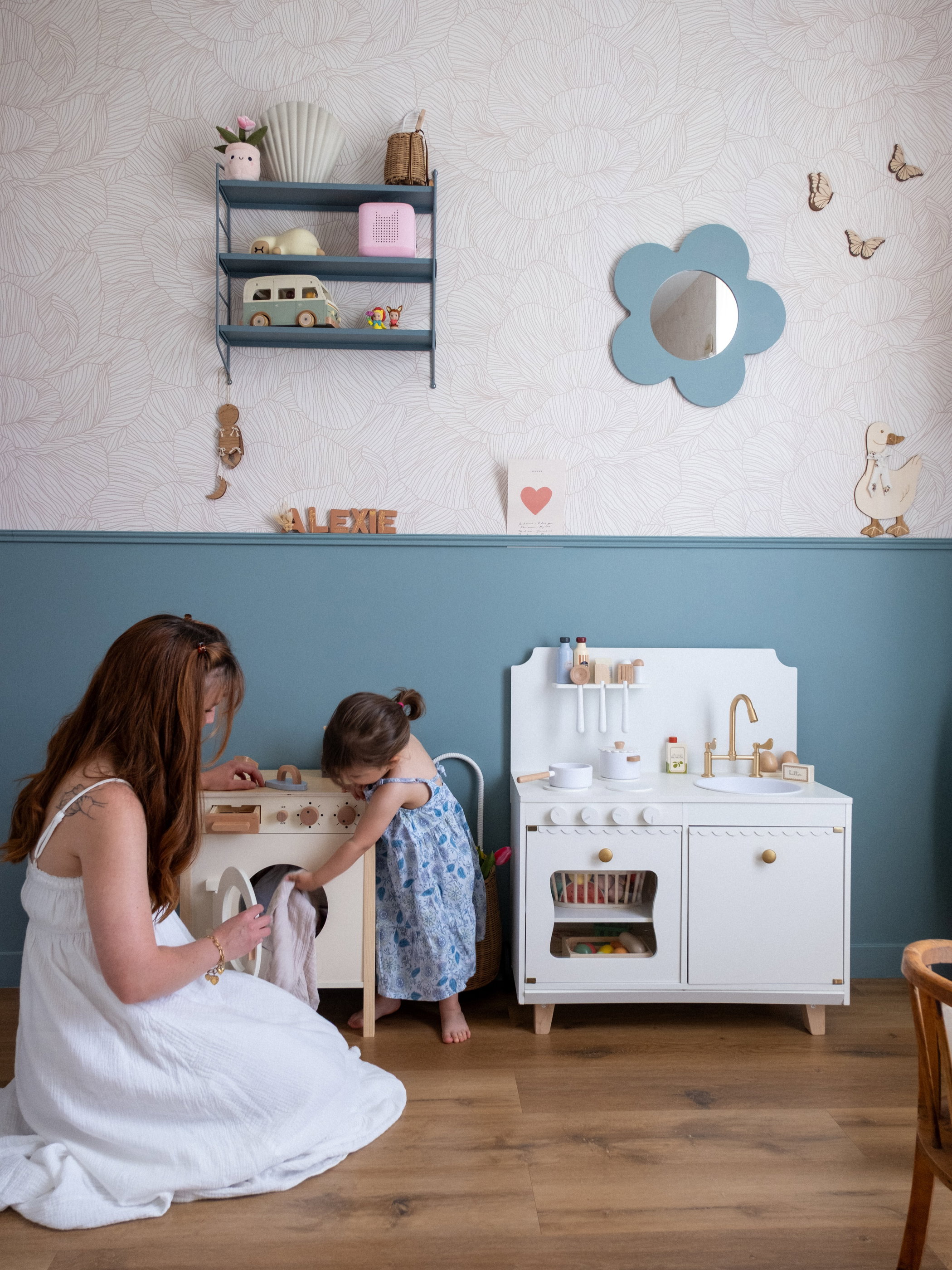A woman and child play with a toy washing machine and kitchen set.