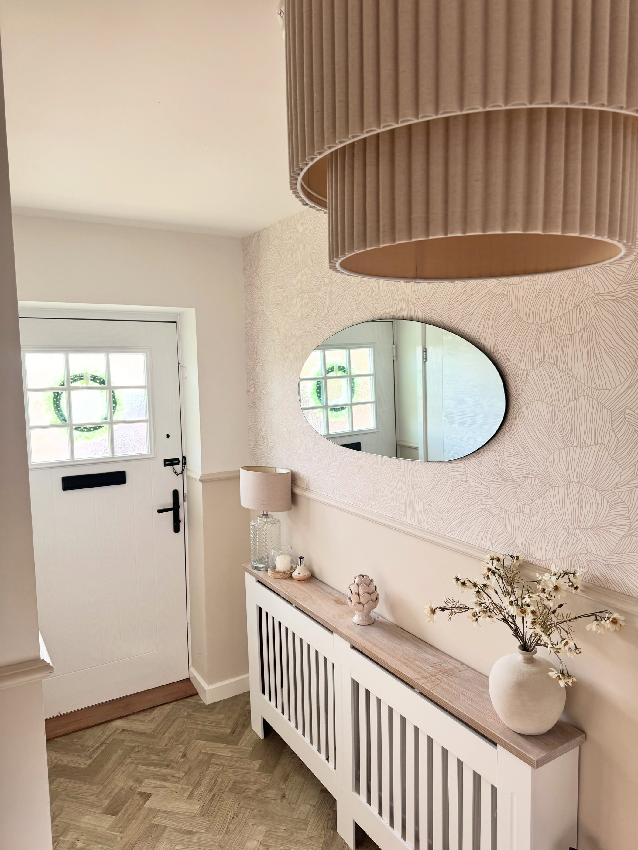 Hallway with white door, oval mirror, and radiator cover with decor.