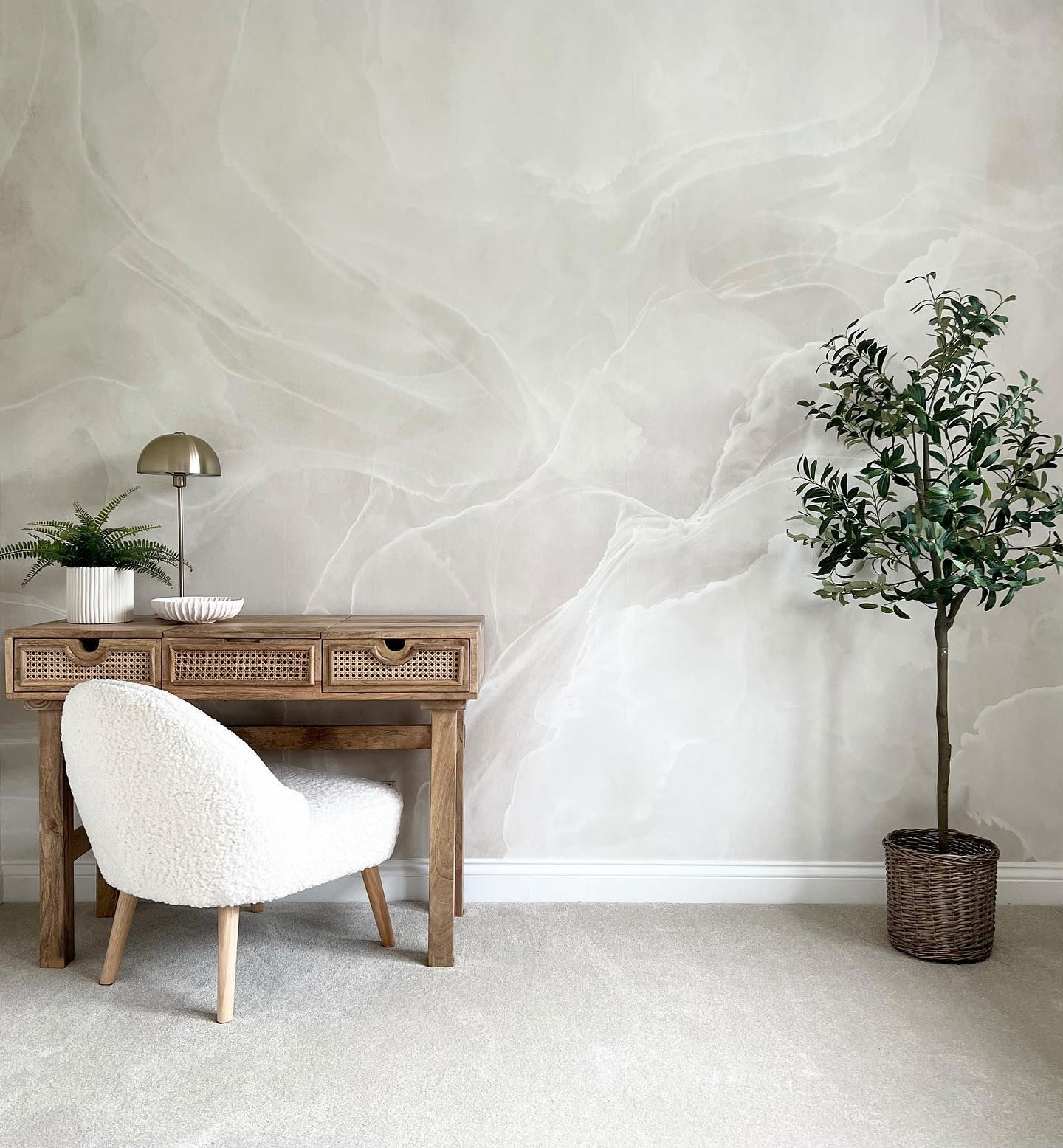 Interno con scrivania in legno, sedia in sherpa, albero in vaso e carta da parati con motivo marmorizzato.