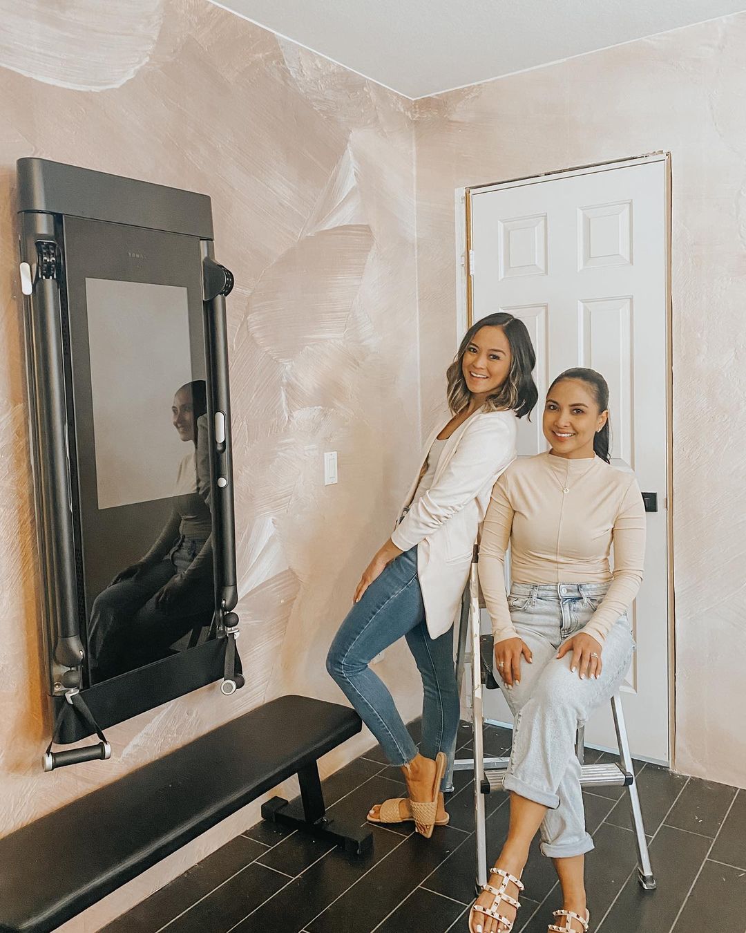 Two women pose in a home gym with a Tonal smart fitness system.