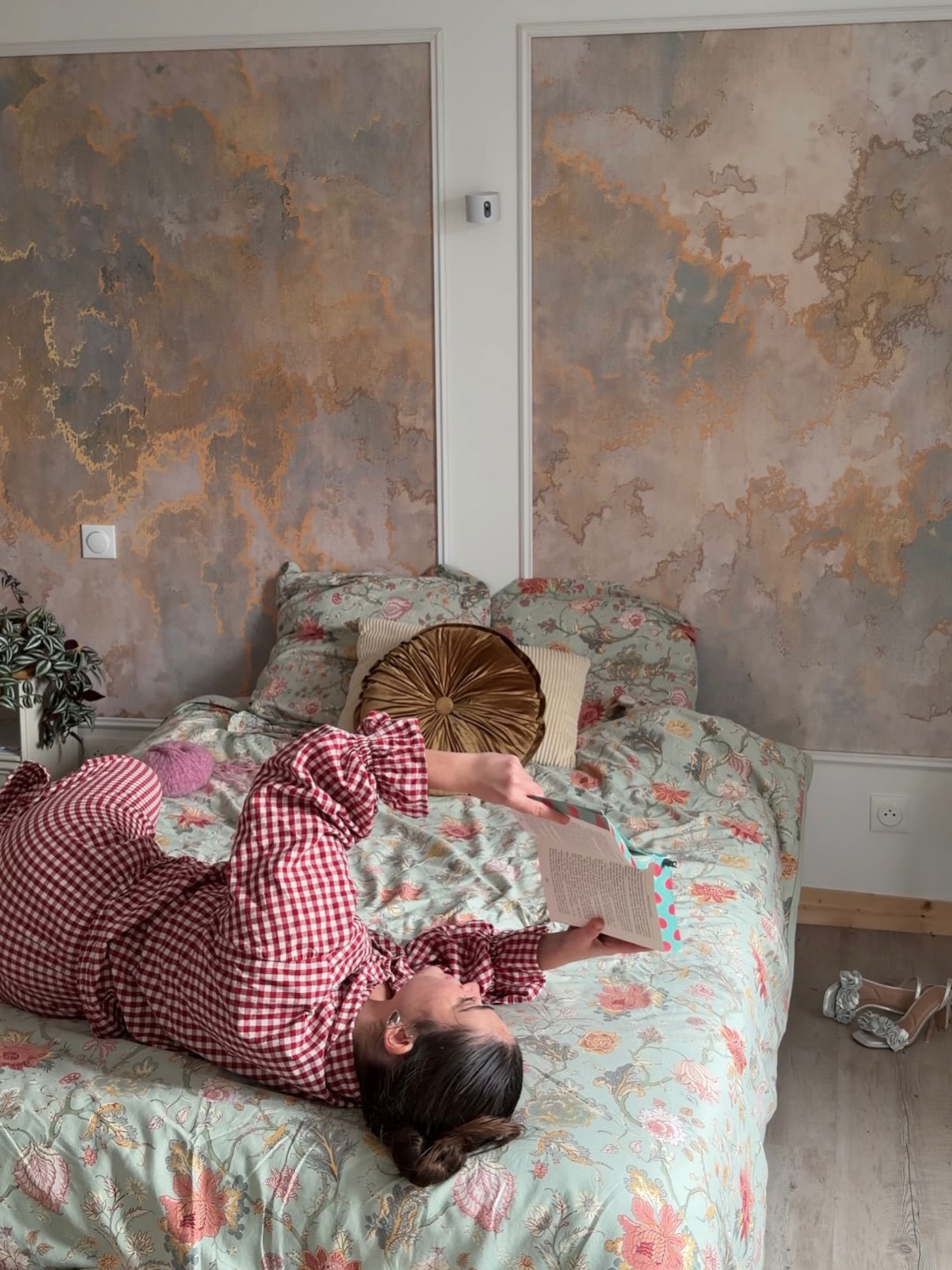 Woman in red gingham pajamas reads on a floral bed.