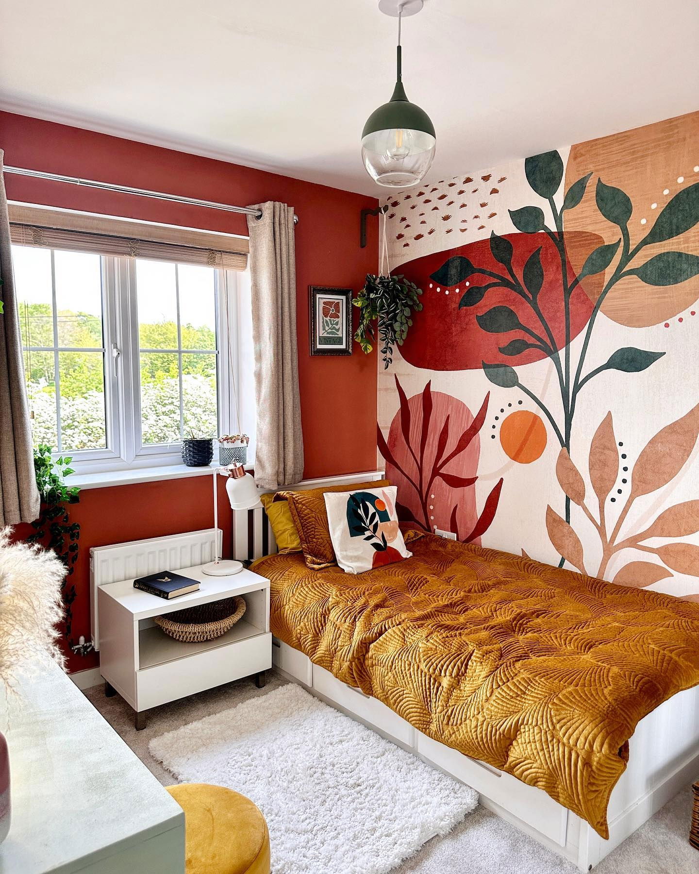 Cozy bedroom with rust-colored walls, botanical mural, and mustard-yellow quilted bedspread.