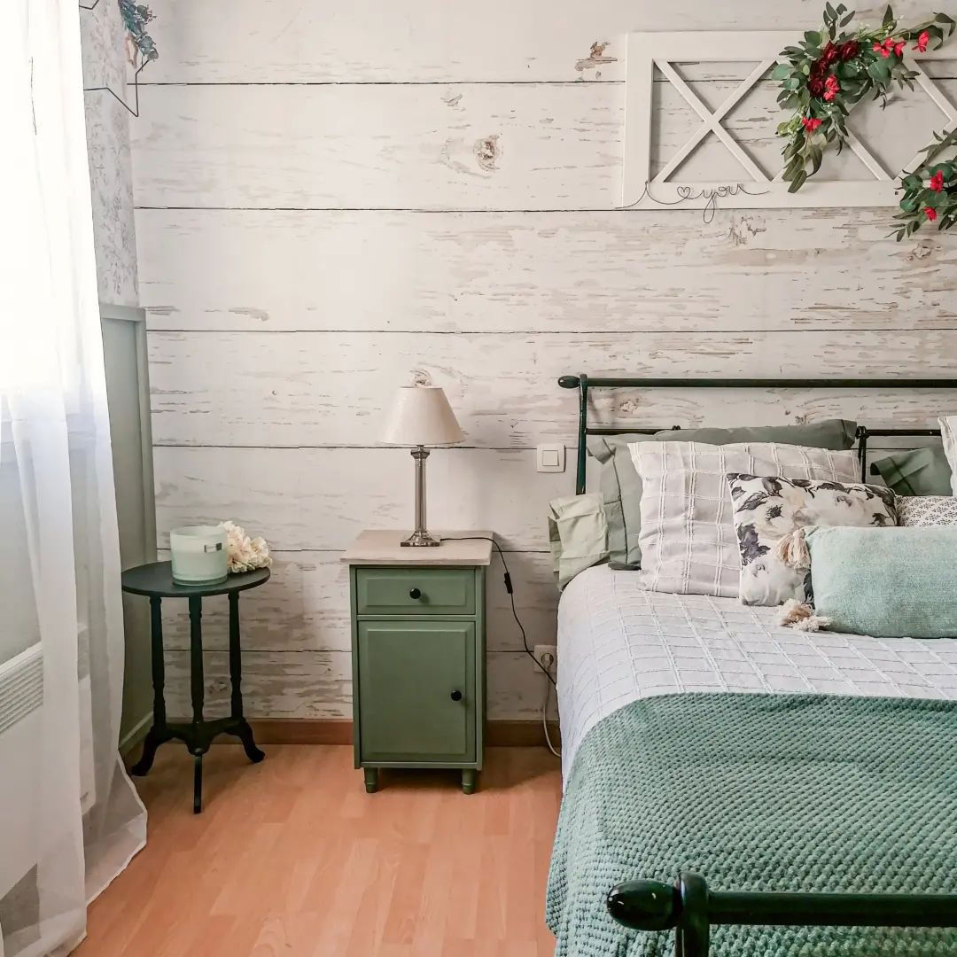 Bedroom with green accents: bed with pillows, green nightstand, and floral wall decor.