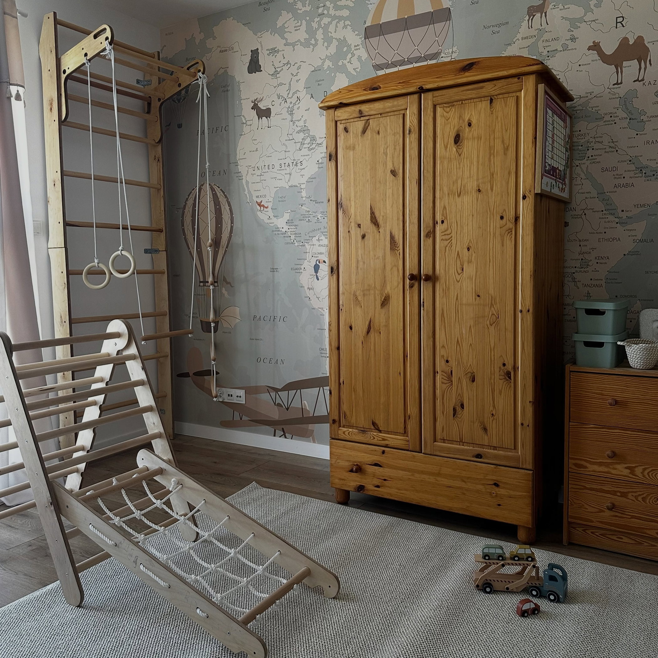 Wooden gym set and wardrobe in a child's room with a world map wallpaper.