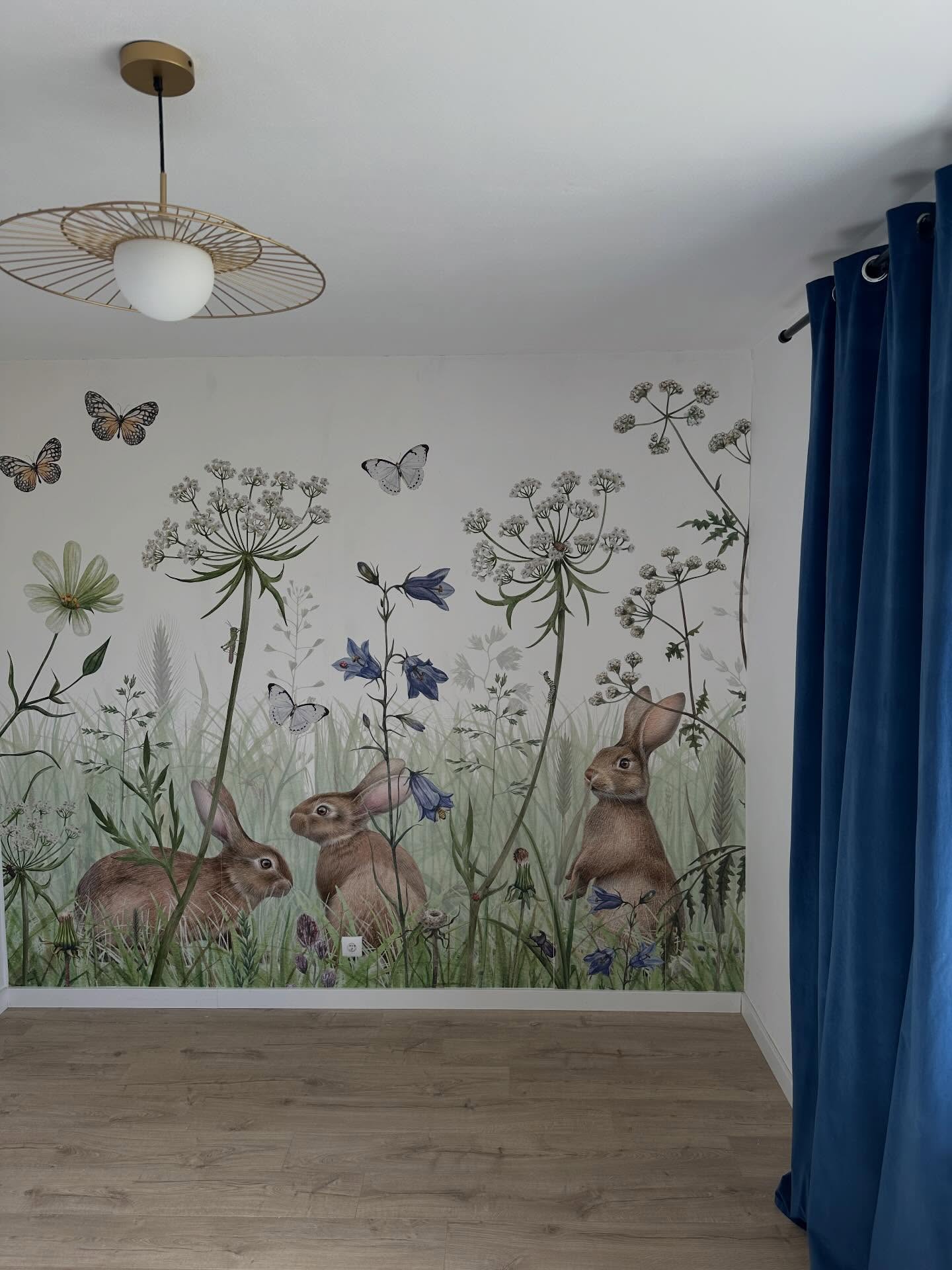 Wanddecoratie met drie bruine konijnen in een bloemrijk grasveld met vlinders. Plafondlamp, blauw fluwelen gordijn.