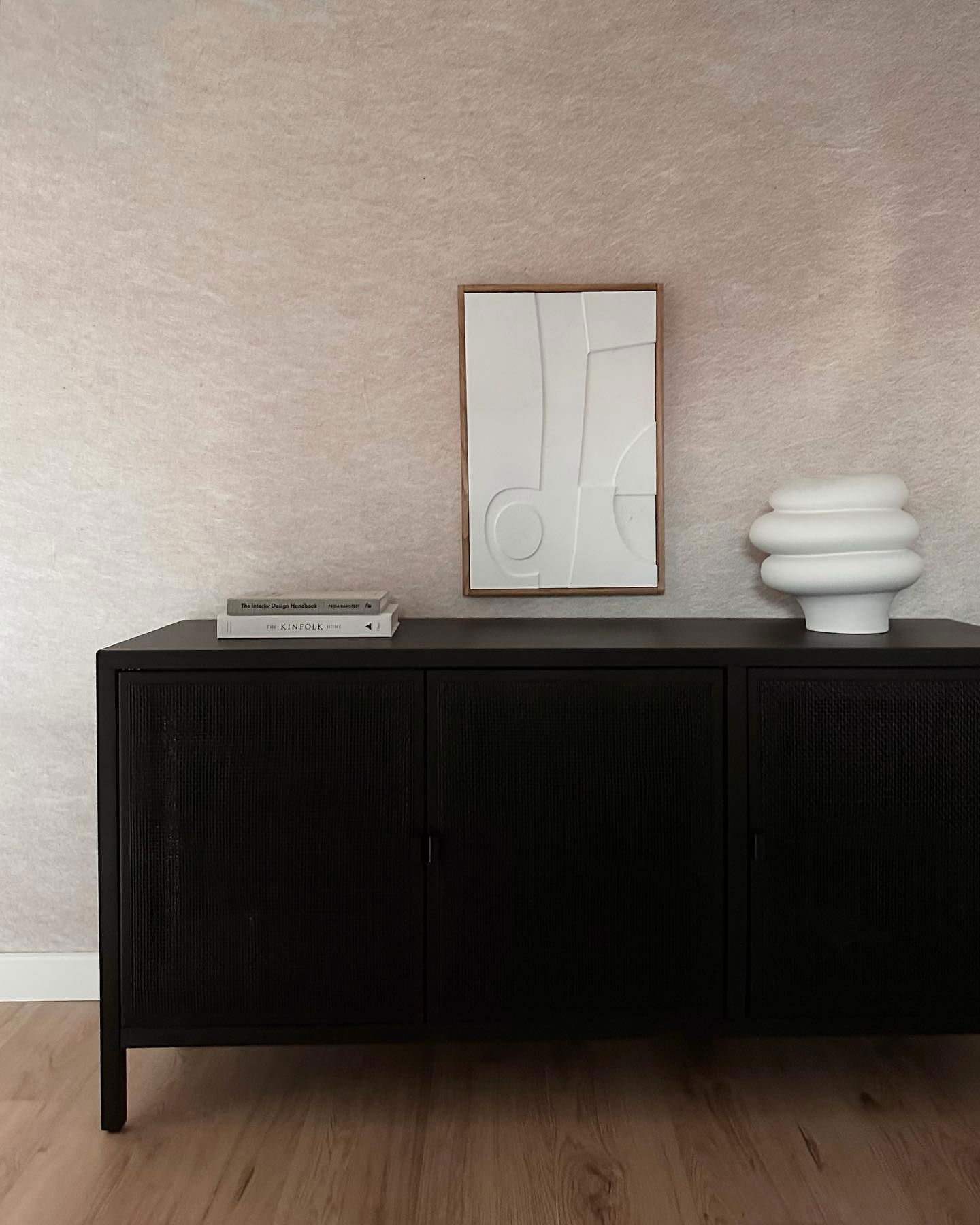 Interior with black cabinet, books, white vase, and framed art.