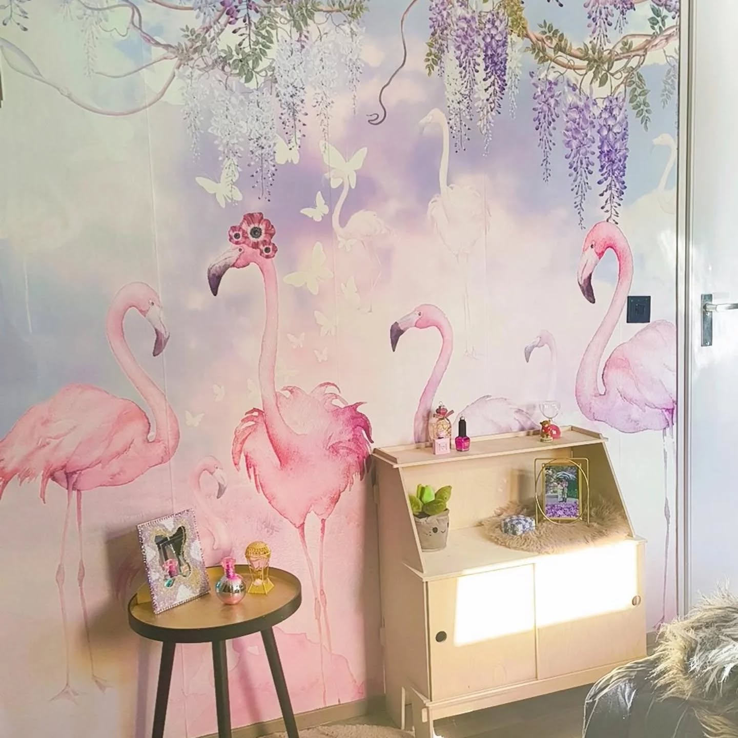 Lyserøde flamingoer og sommerfugle på et vægmaleri med et lille træskrivebord og et sidebord.