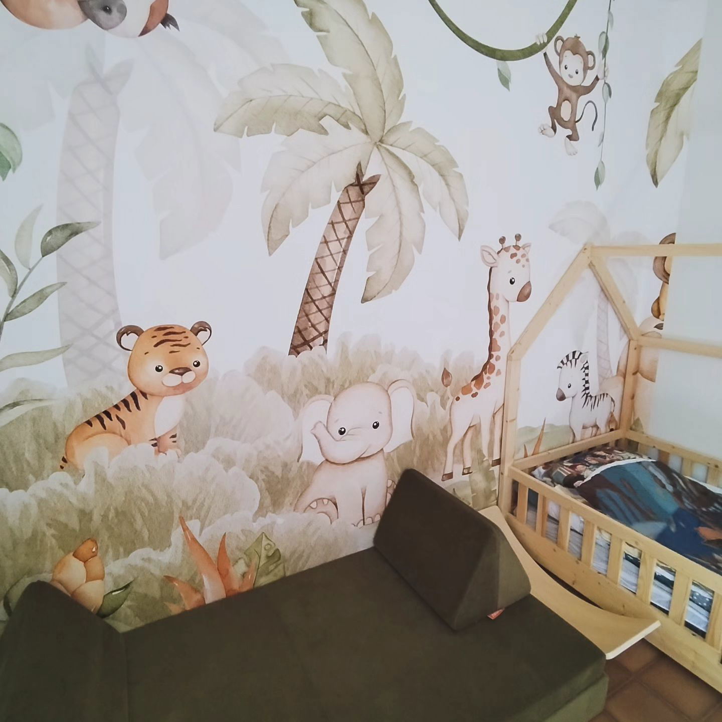 Child's room with jungle-themed wallpaper, wooden bed, and green modular sofa.