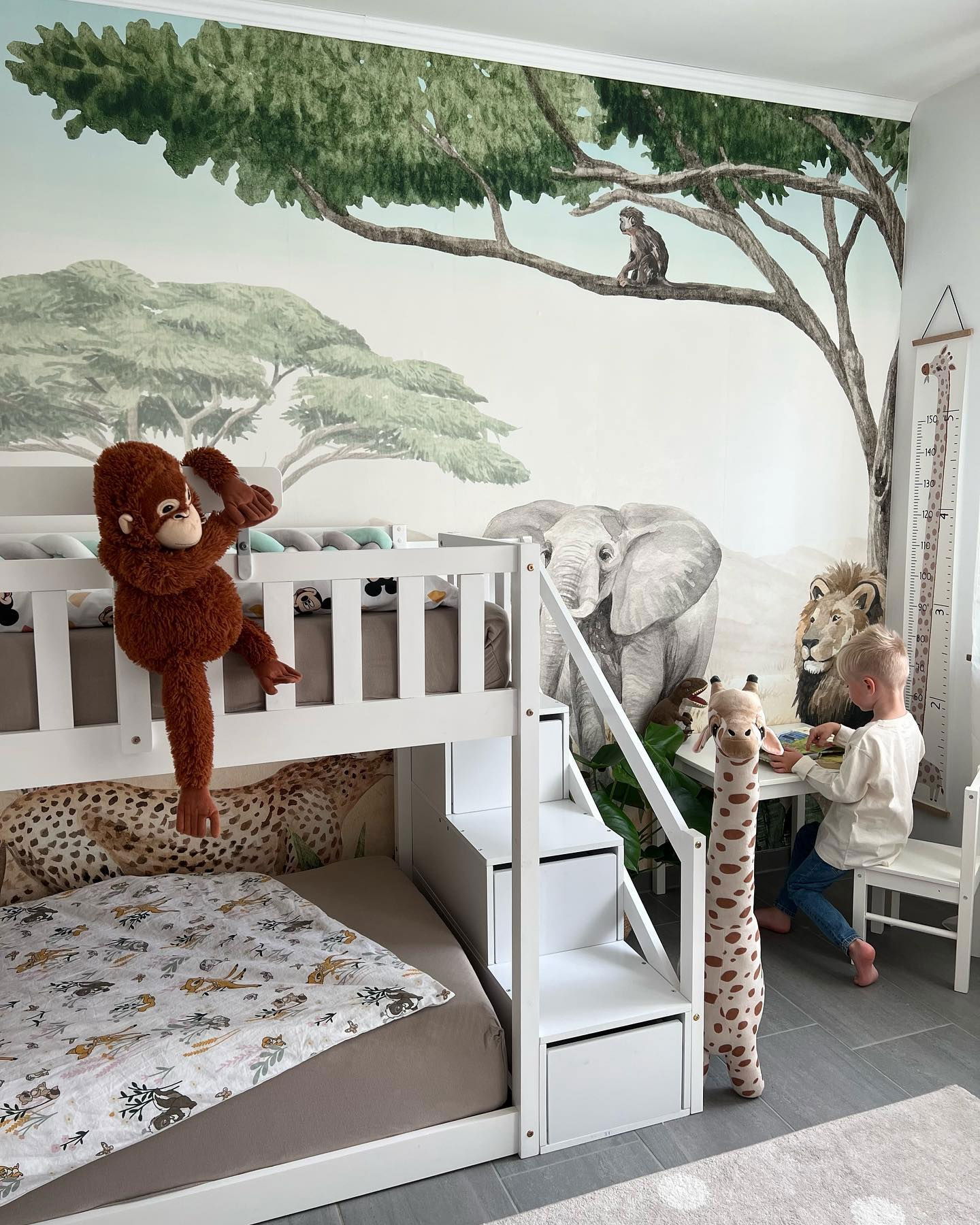 Child's bedroom with safari mural, white bunk beds, and stuffed animal decor.