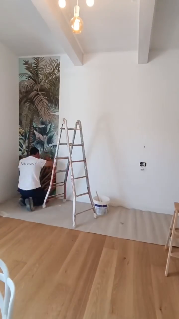 A Valpaint worker installs a tropical wallpaper mural in a bright room.