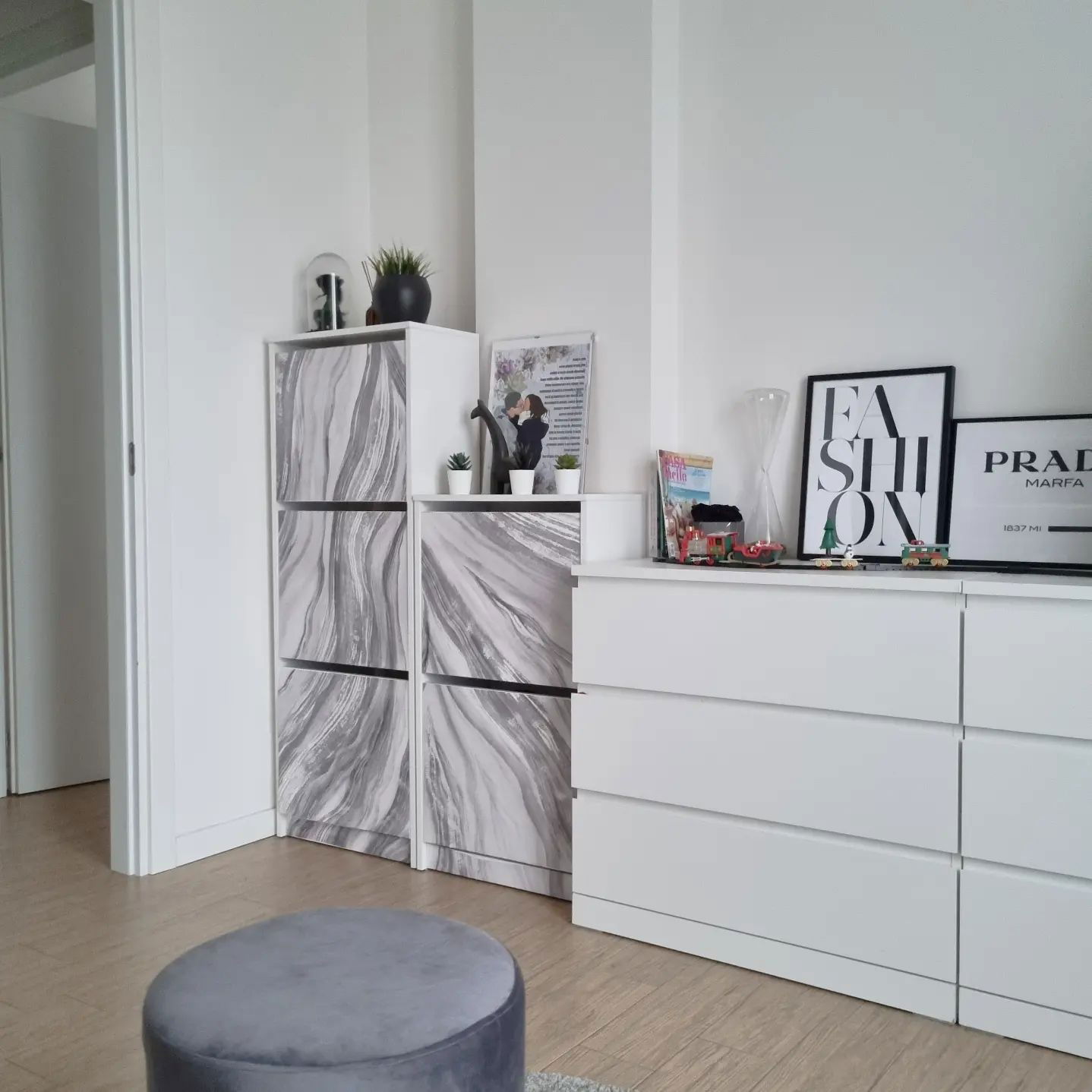 Innenansicht von weißen Schränken mit Marmormustertüren sowie einer weißen Kommode mit gerahmter Kunst.