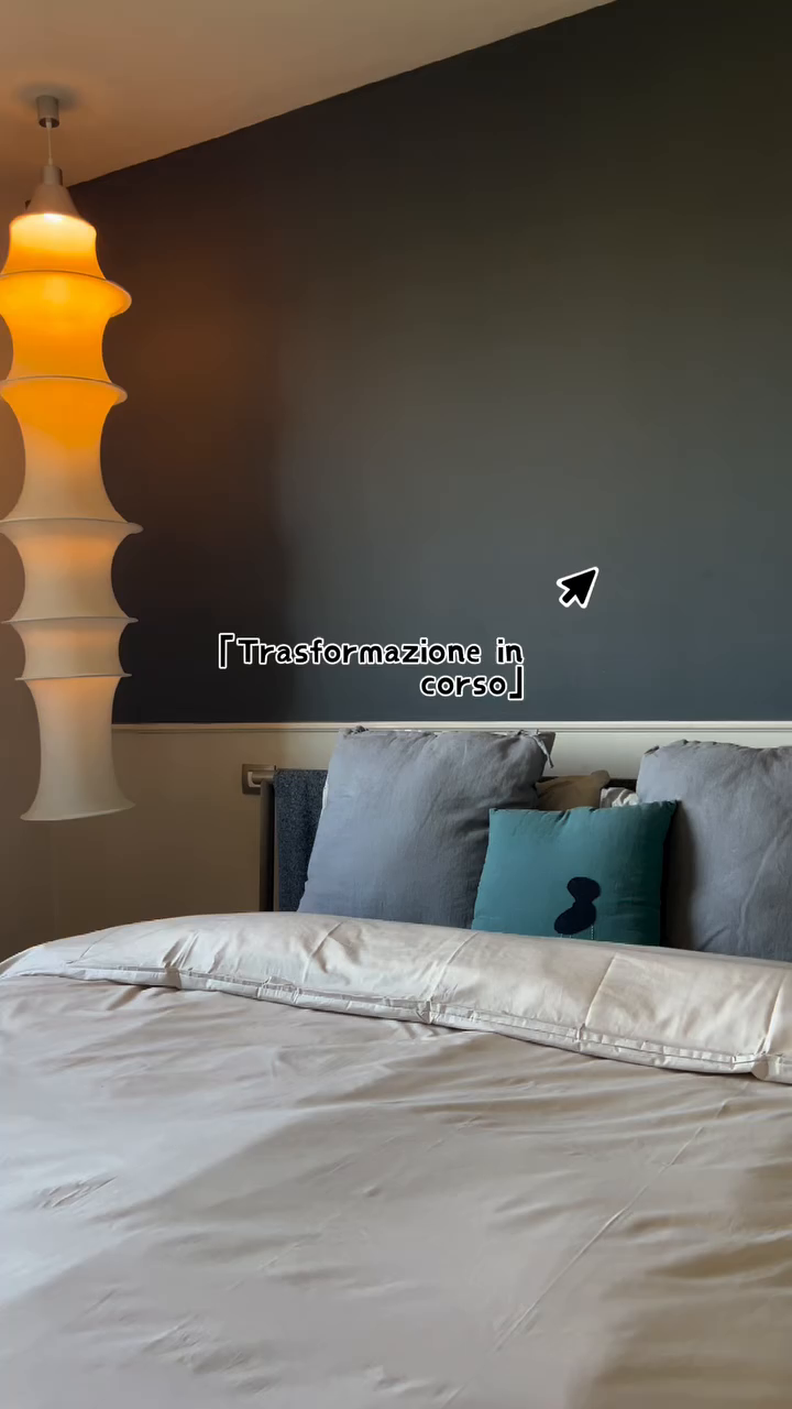 Bedroom with gray bedding, blue pillows, and a modern orange and white pendant lamp.