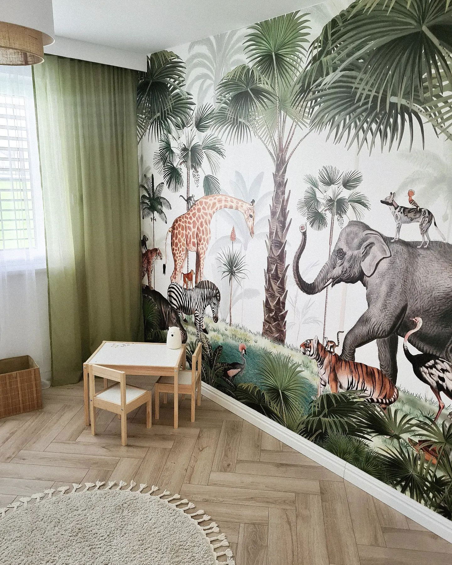 Child's room with jungle animal wallpaper, small table and chairs, round rug, and green curtains.