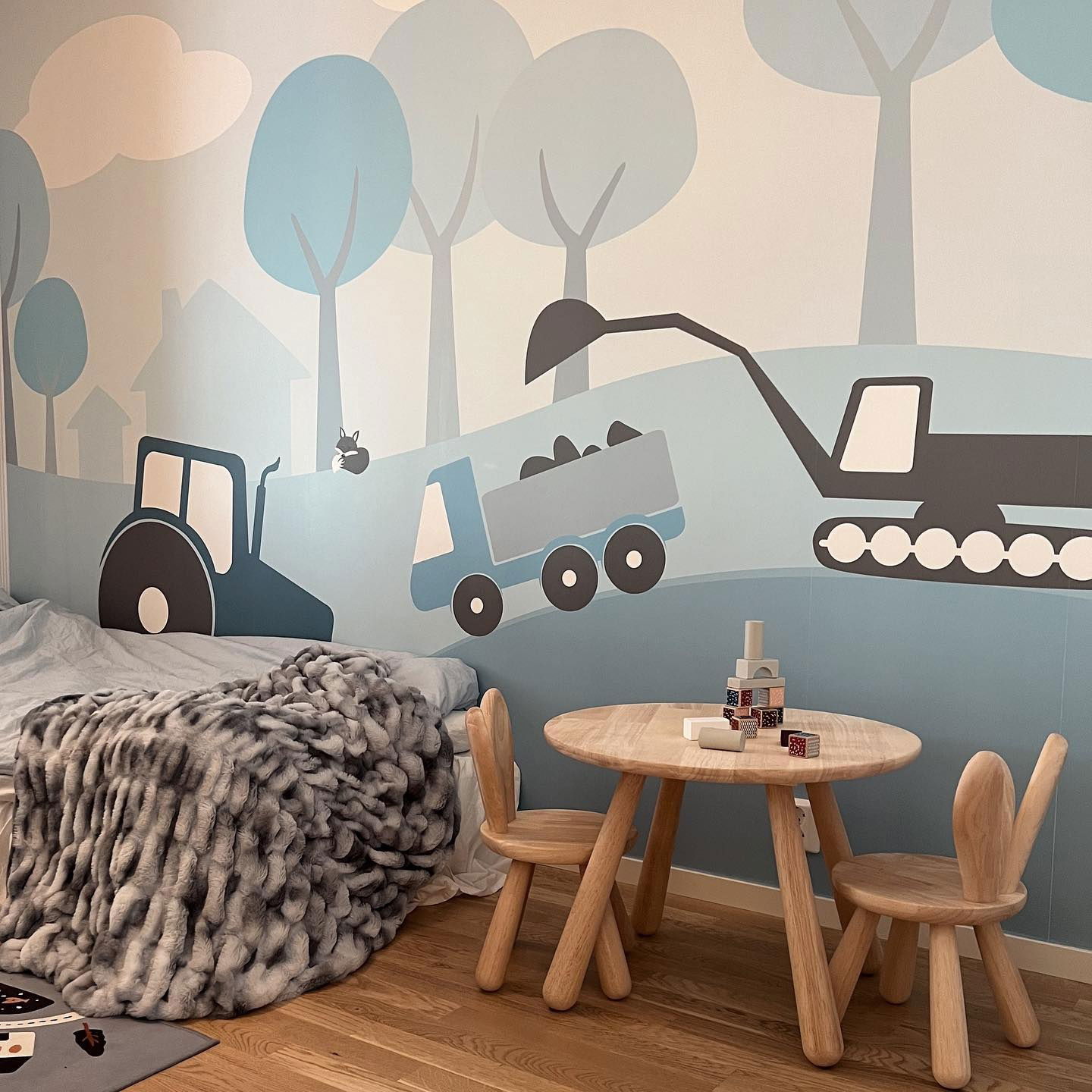 Kinderzimmer mit Baumalerei, Holztisch und Hasenstühlen sowie Bett mit Fellüberwurf.