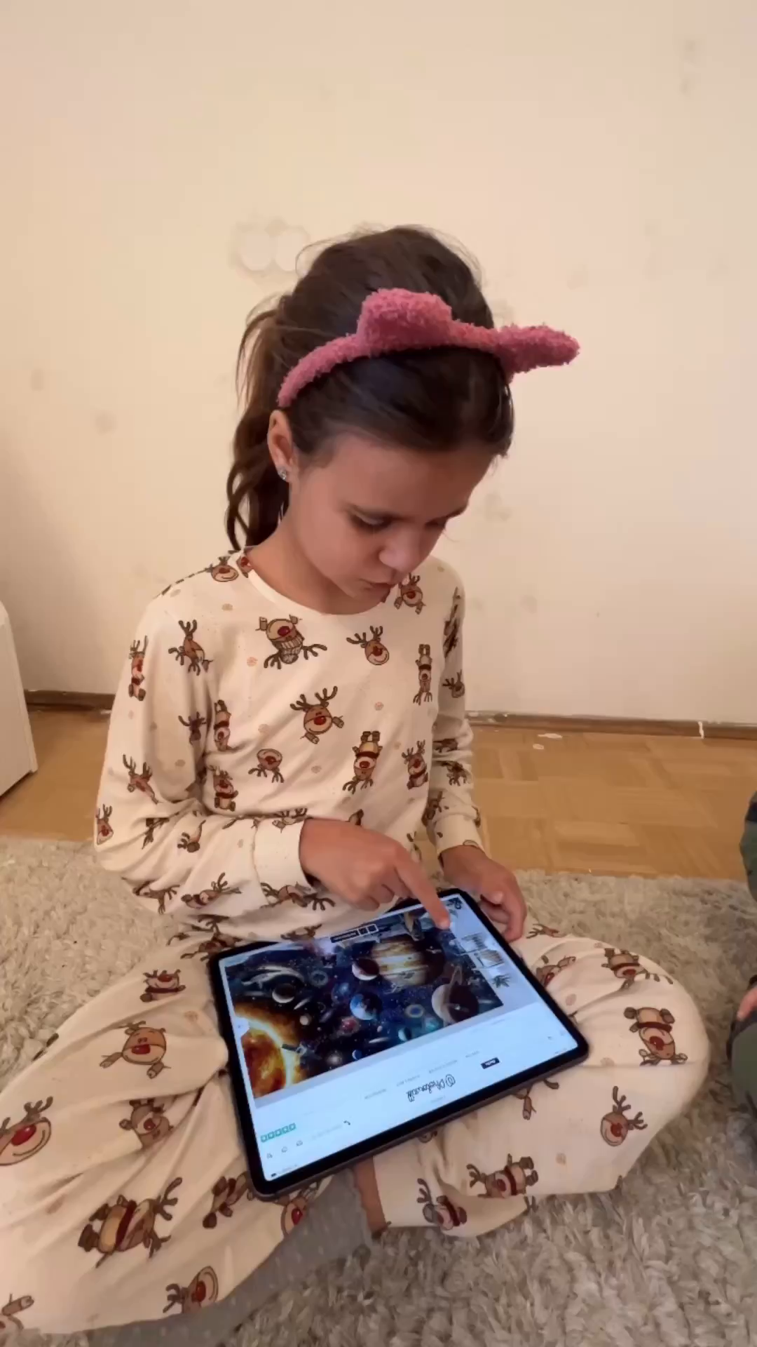 Girl in reindeer pajamas using a tablet. The screen displays an image of the solar system.