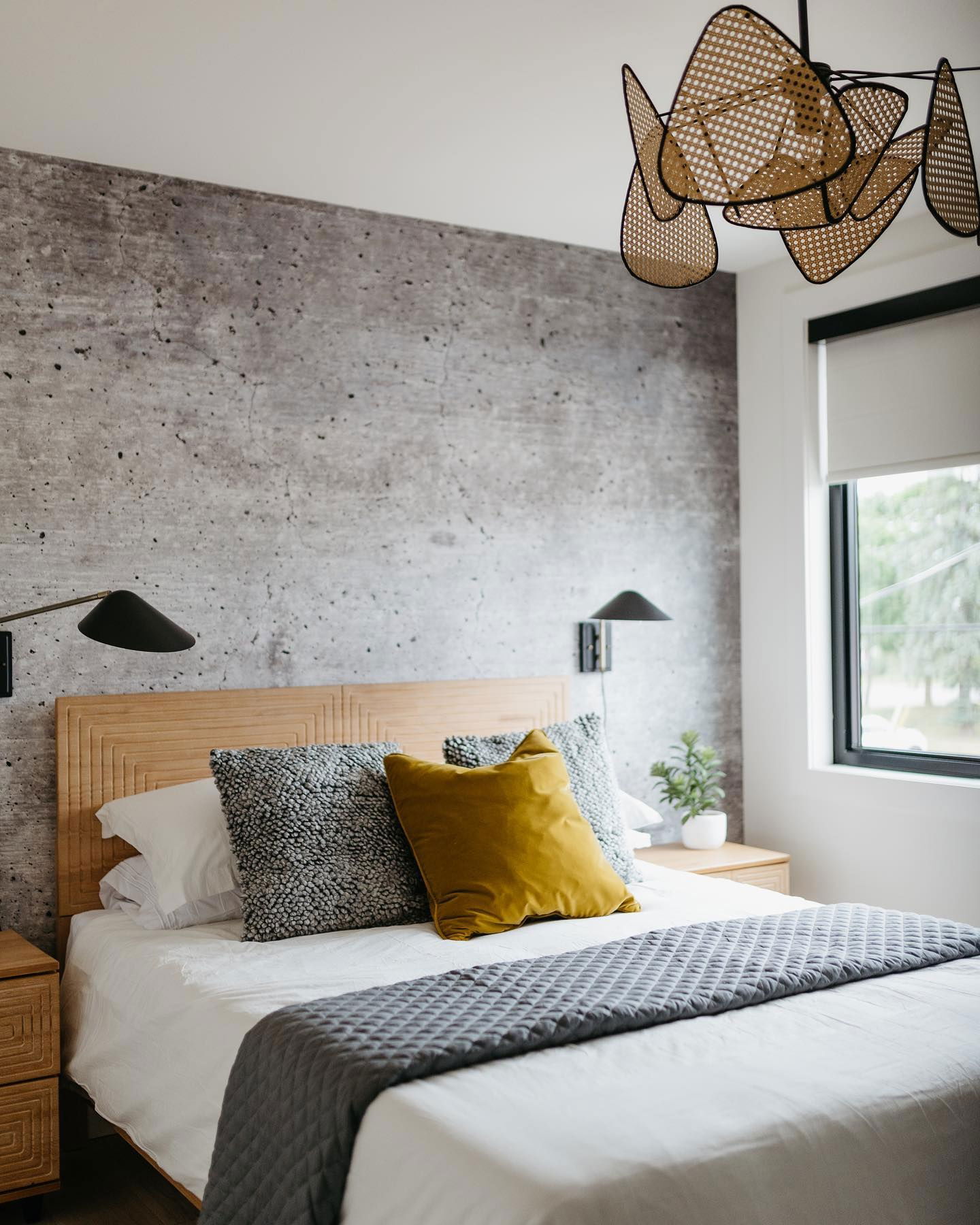 Bedroom with concrete accent wall, wood headboard, and woven chandelier.