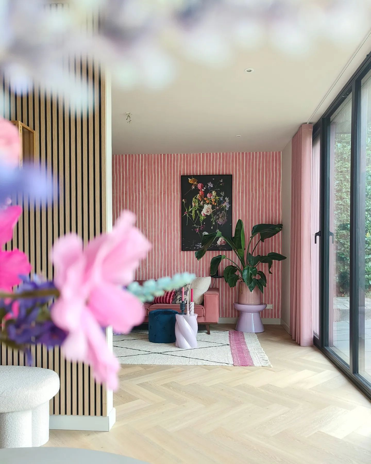 Living room with pink striped walls, floral art, pink sofa, and large windows.