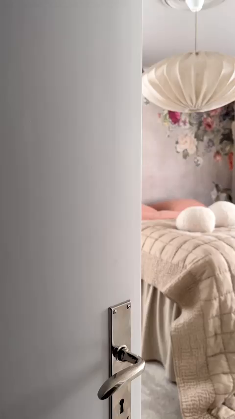 Open door reveals bedroom with floral wallpaper, quilted bedspread, and white pendant light.