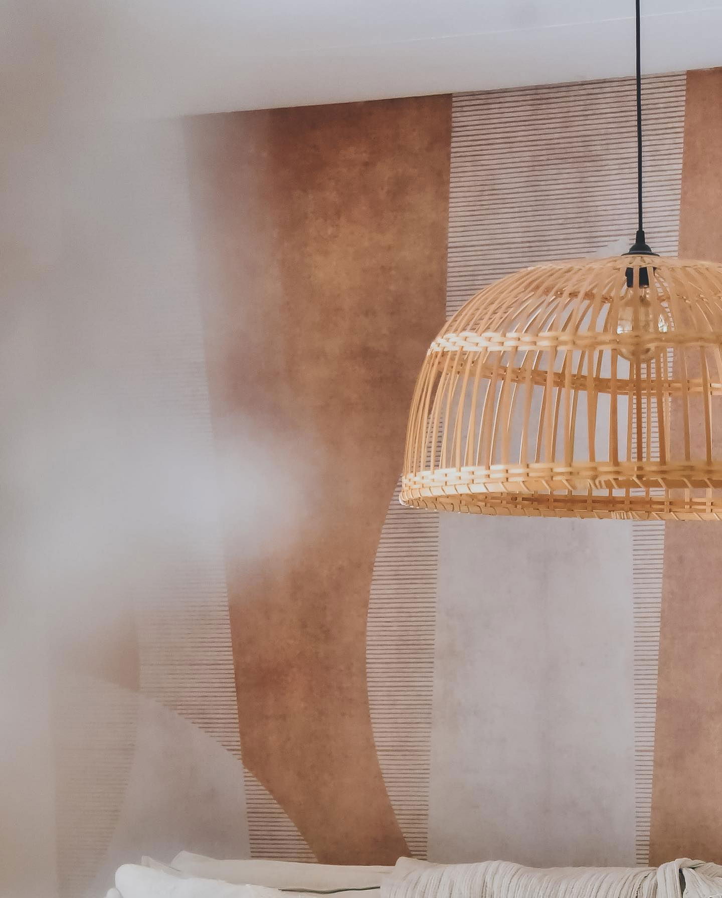 Hanglamp van wicker tegen een behang met patroon.