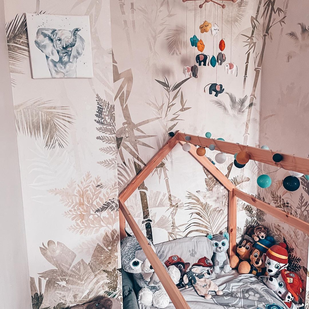 Child's room with jungle wallpaper, wooden house bed filled with stuffed animals, and elephant art.