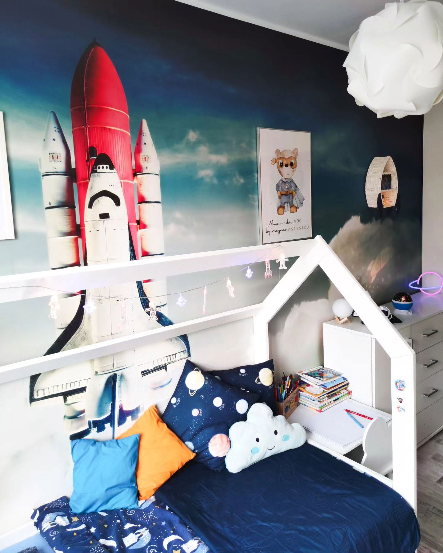 Child's bedroom with space-themed wallpaper, house frame bed, and cloud pillow.