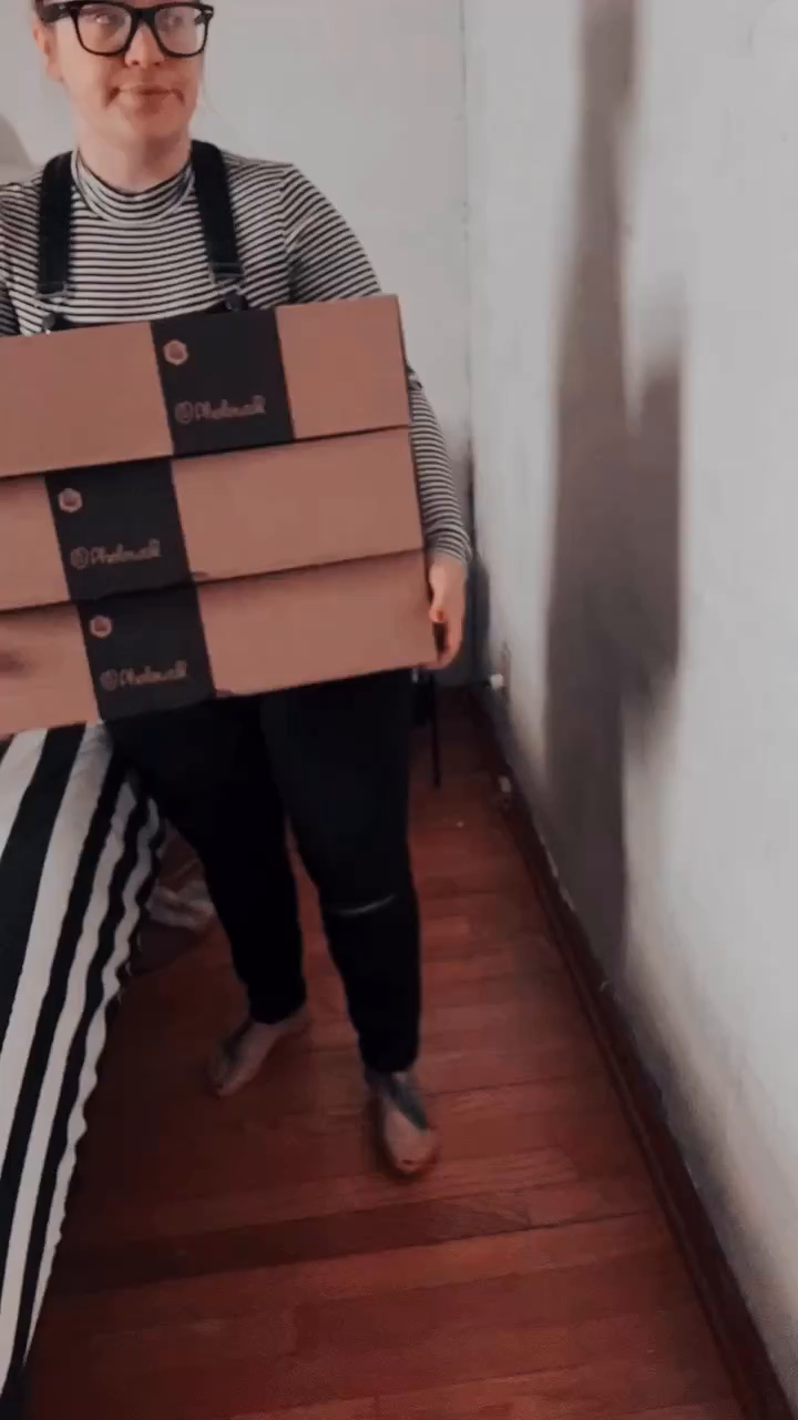 Person carrying three Photomall branded boxes in a hallway.