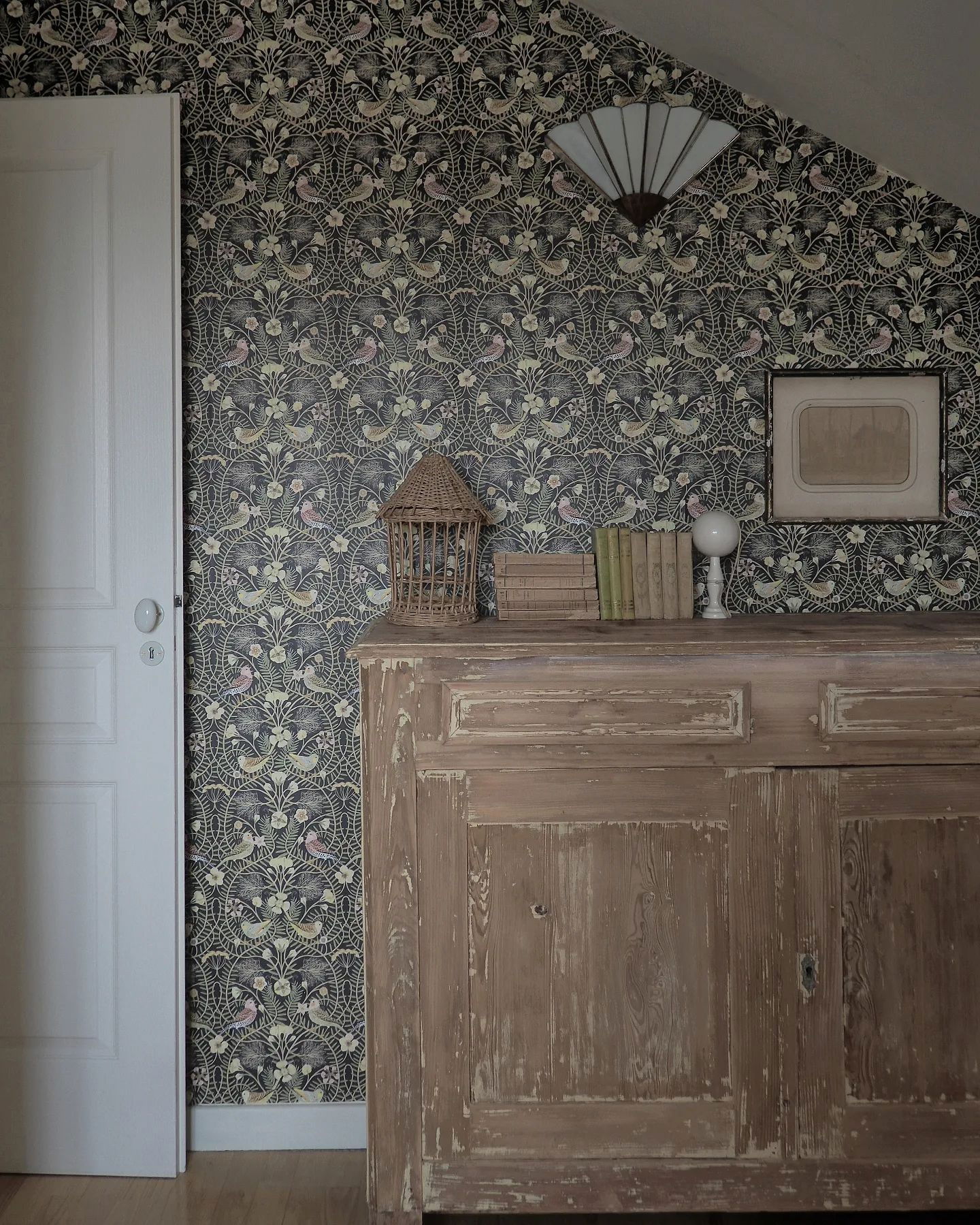 Interior with floral bird wallpaper, white door, and distressed wood cabinet.