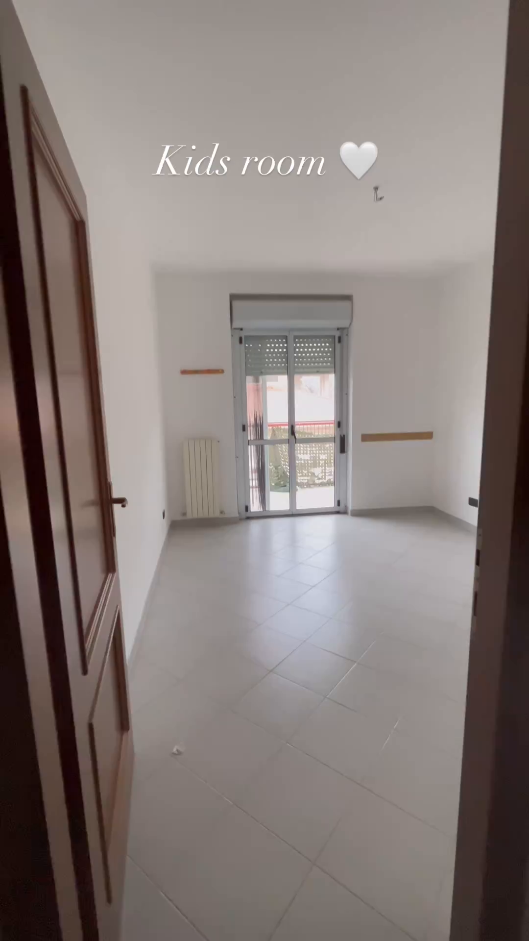 Empty kids room with white walls, gray tile floor, and balcony access.