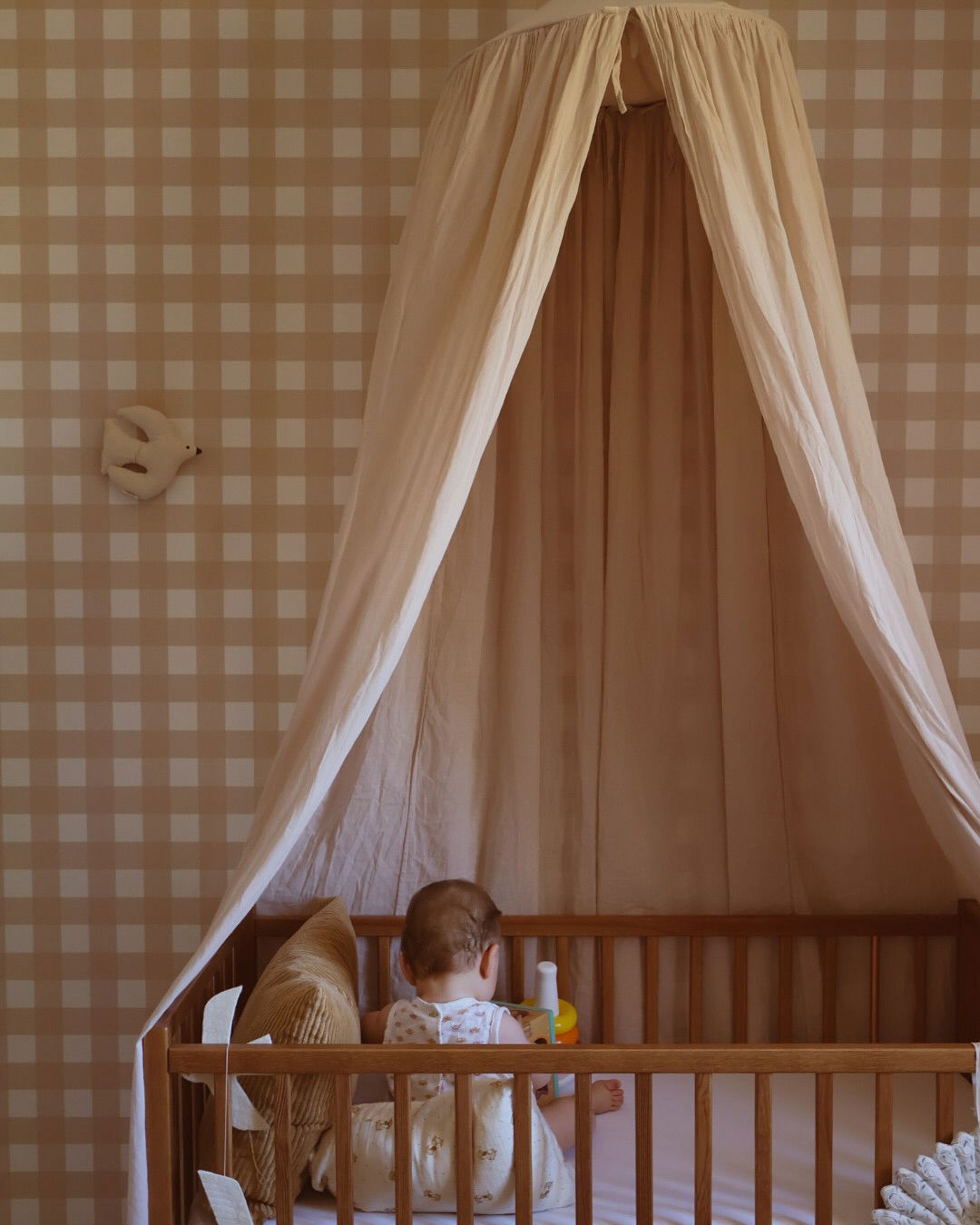 Baby i tremmeseng med baldakin, ginghamtapet og duevægdekoration.