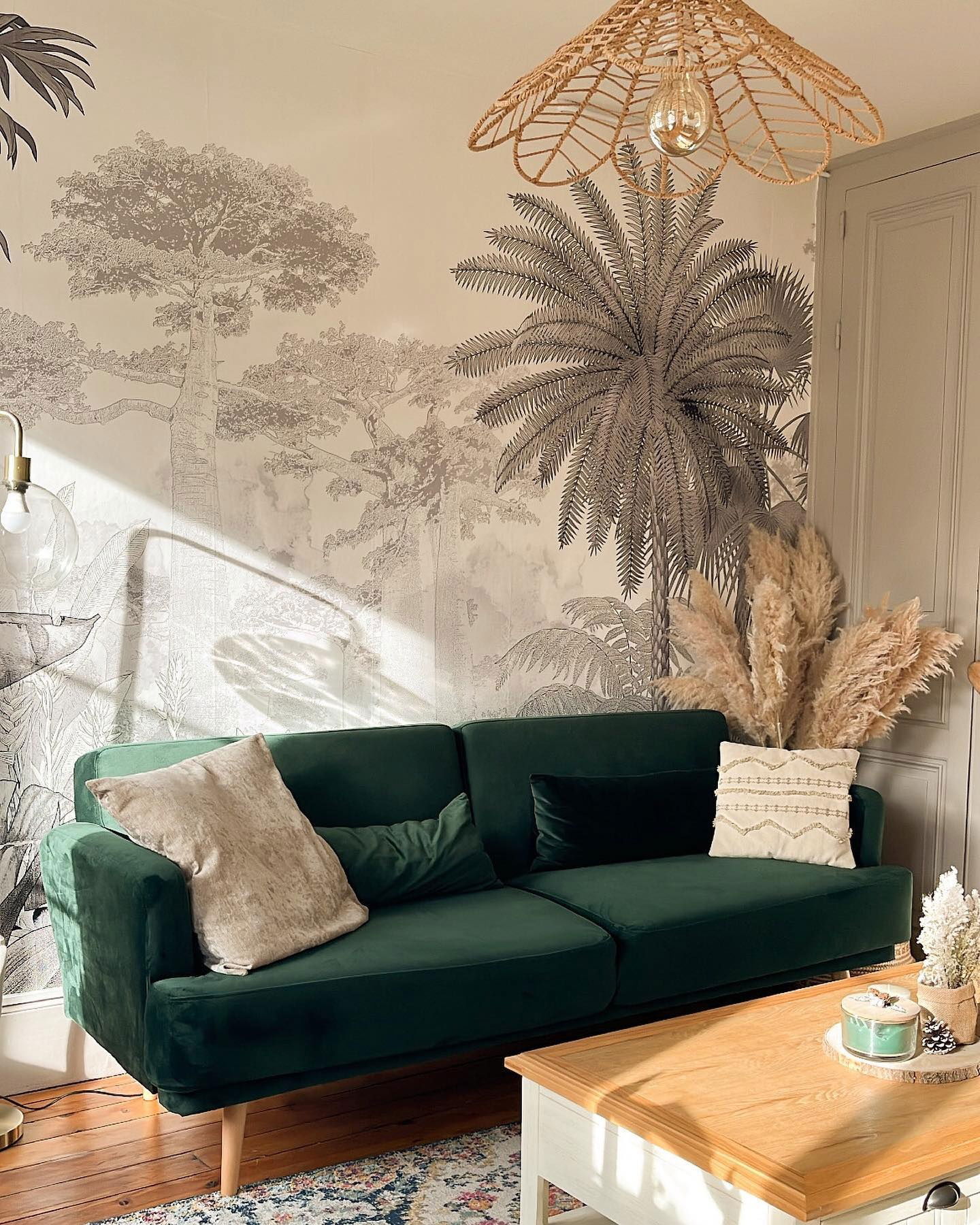Salon z zieloną aksamitną sofą, wzorzystą tapetą i plecioną lampą wiszącą.