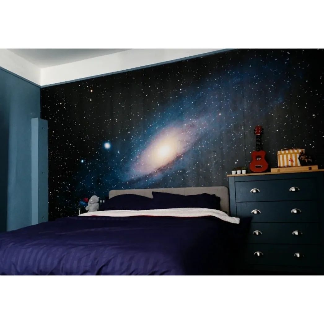 Bedroom with galaxy wall mural, blue bedding, and matching dresser with a red ukulele on top.