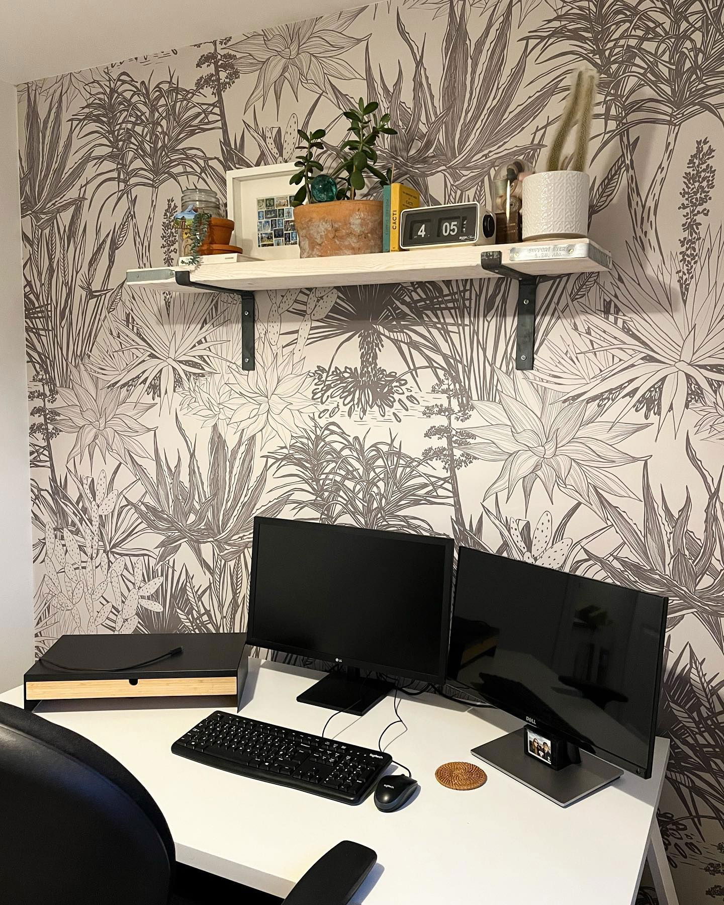 Home office setup with dual monitors, keyboard, and shelf against botanical wallpaper.