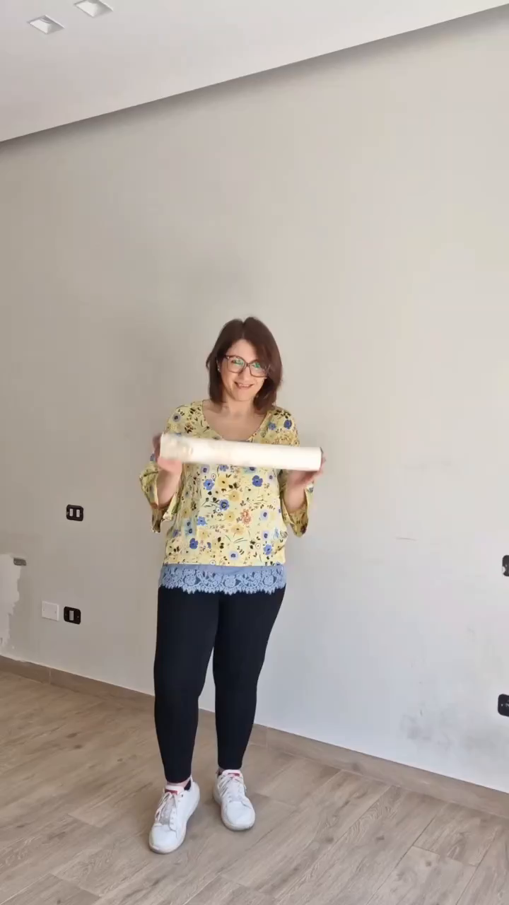 Woman holding a roll of wallpaper in front of a blank wall.