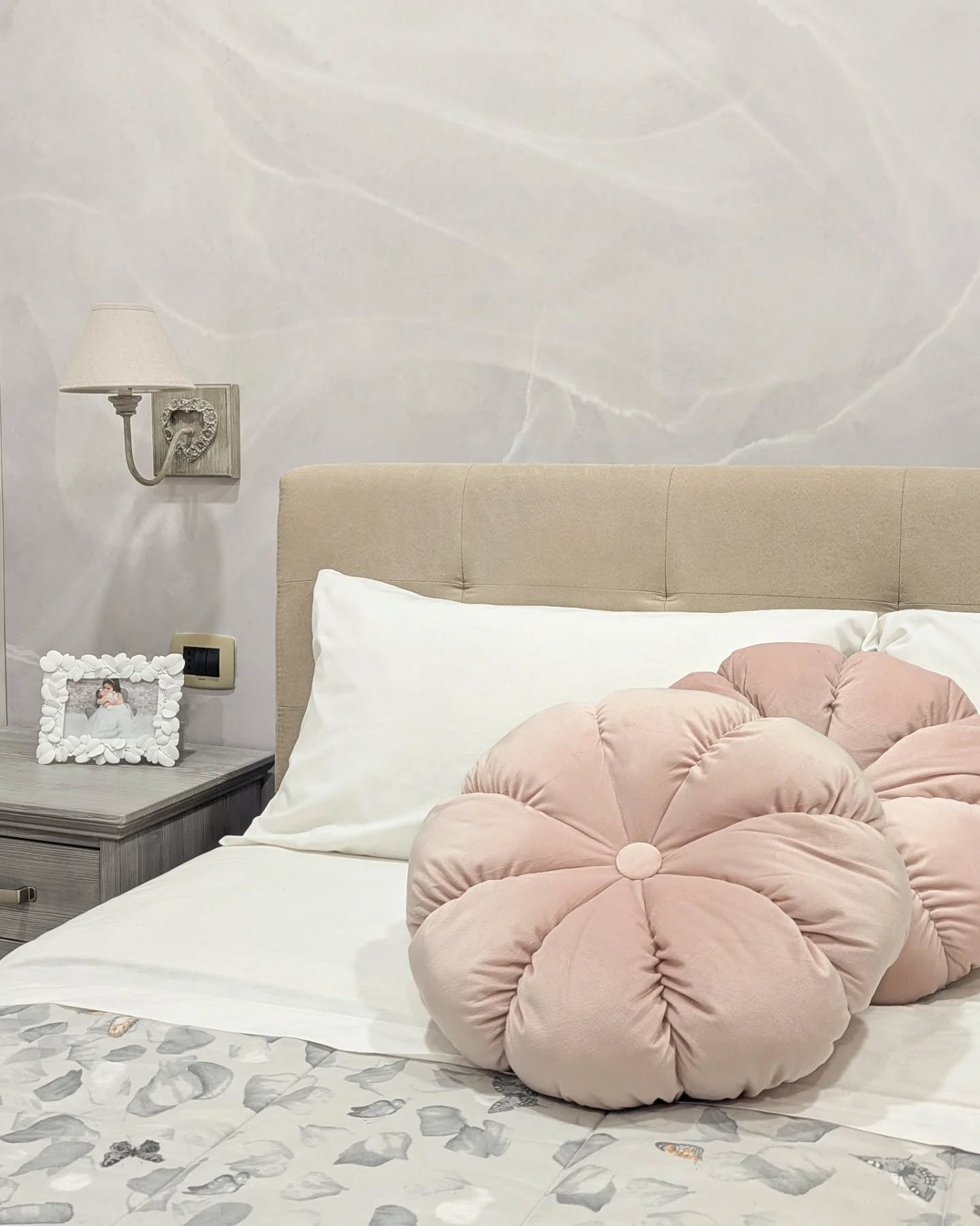 Scène de chambre avec des coussins ronds en velours rose sur un lit avec des draps blancs.