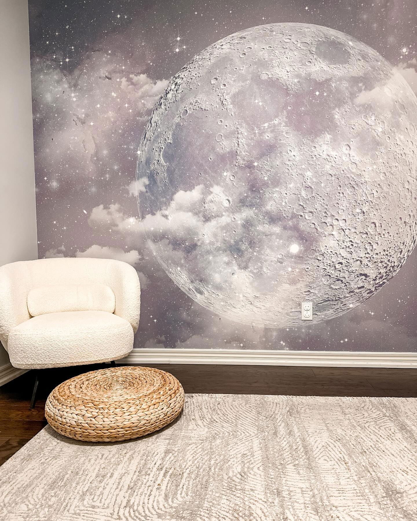 Intérieur avec une murale murale de lune, une chaise blanche, un pouf tissé et un tapis à motifs.