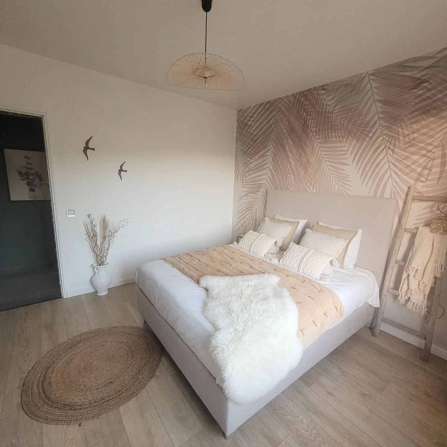 Dormitorio con tonos neutros, papel tapiz de hojas de palma y una alfombra de yute.