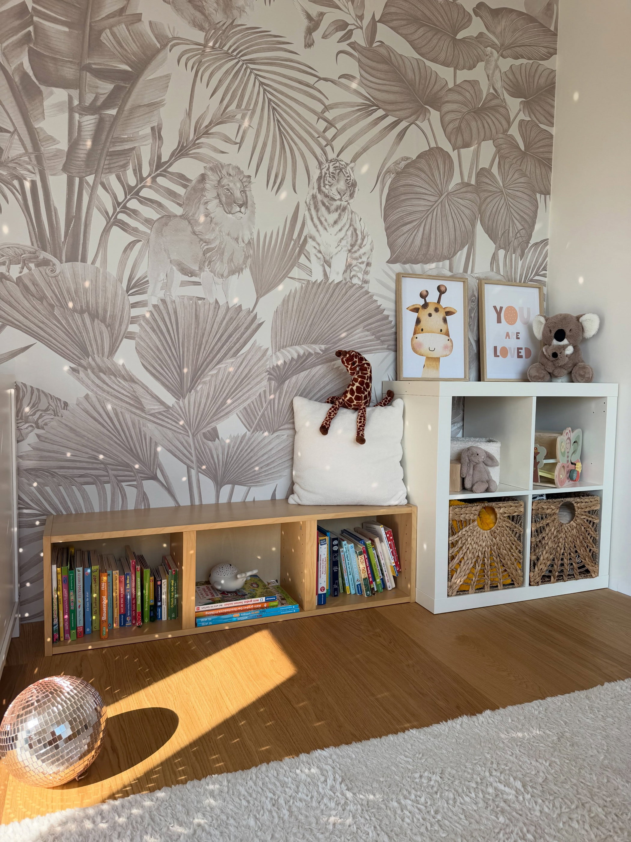 La chambre d'un enfant avec un papier peint sur le thème de la jungle, une étagère en bois et des peluches.
