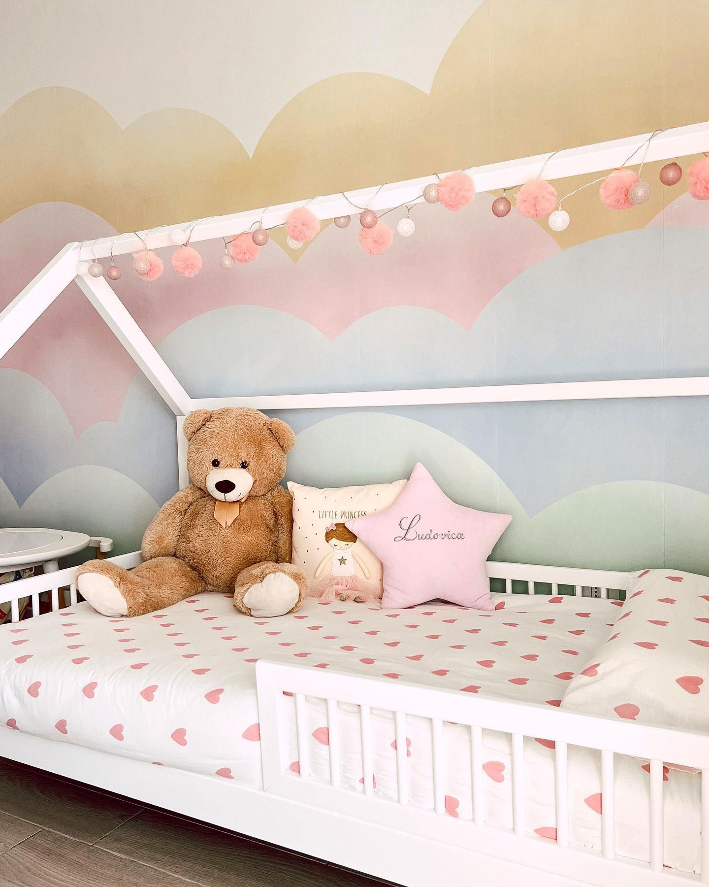 Child's white house bed with heart sheets, teddy bear, and pink star pillow.