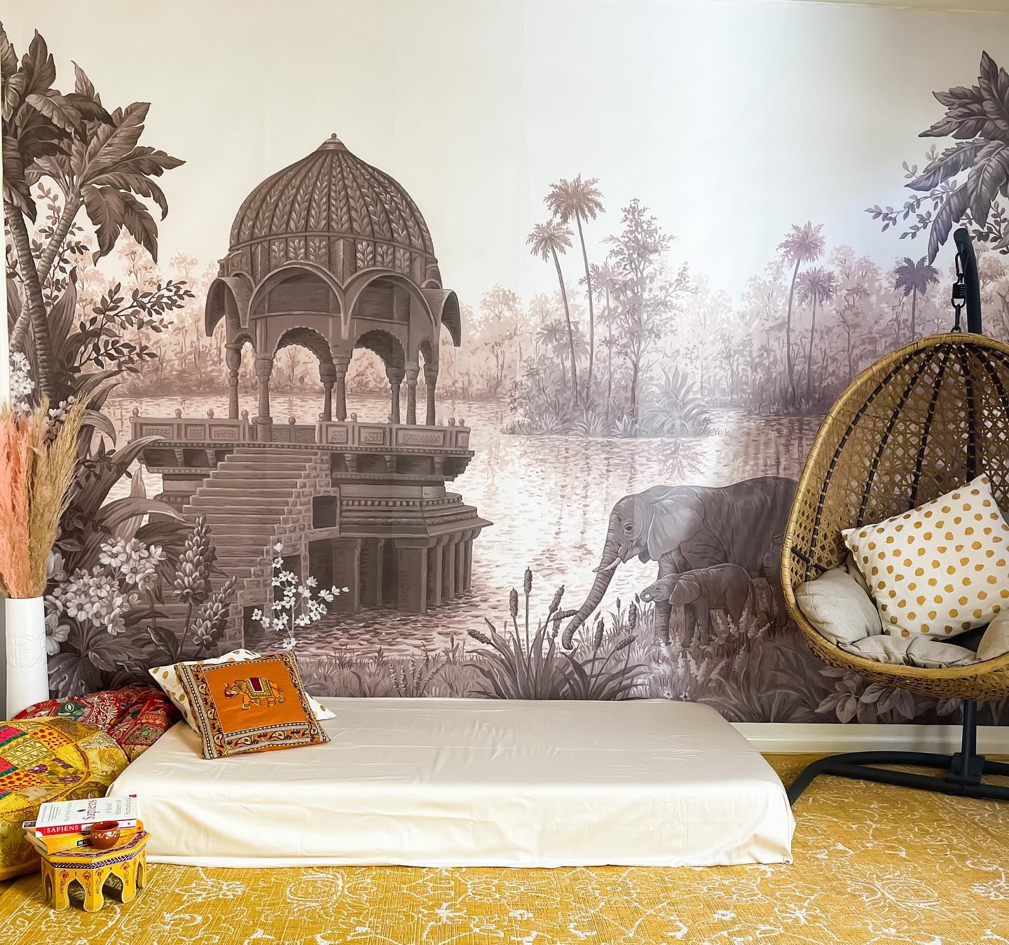 Eclectic room with elephant mural, floor mattress, and hanging chair.
